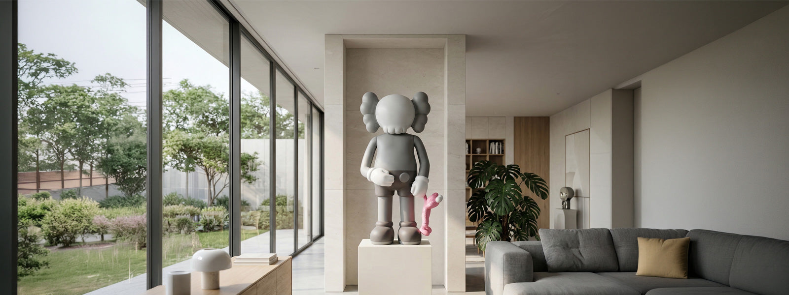 Large gray and white Iconify sculpture with rounded ears holding a small pink figure on a white pedestal in a modern living room with tall windows.