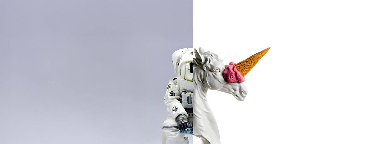 Astronaut figure with a white unicorn head replacing the helmet and a pink ice cream cone on its horn against a split grey and white background.