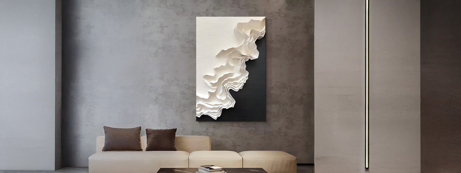 Layered black-and-white cardboard art with sculptural wave-like texture mounted on a gray concrete wall above a beige sofa with brown cushions.