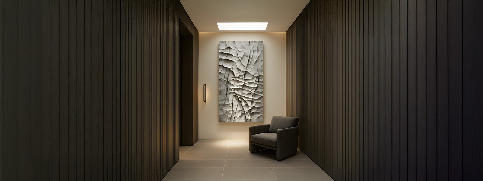 Large textured white relief wall art with organic cracked patterns in a minimalist hallway featuring dark fluted wood paneling and a dark armchair.