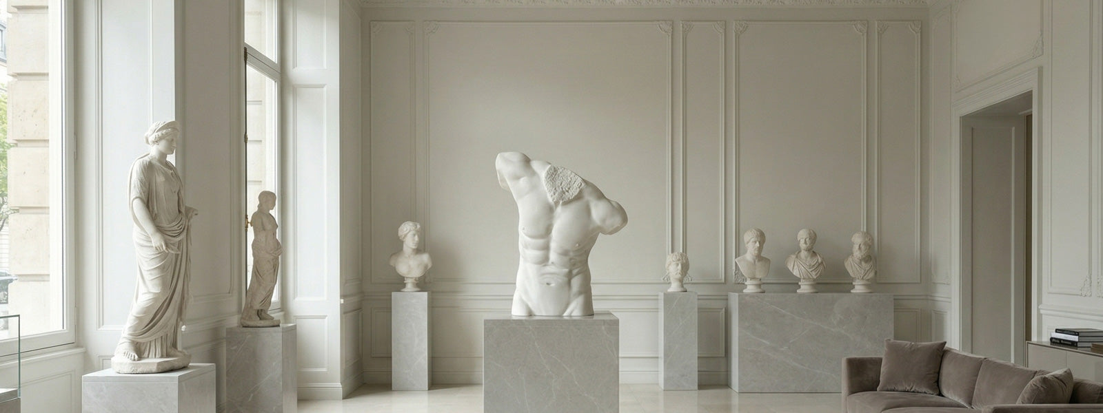Gallery room with marble sculptures including a draped female figure, a muscular male torso on a stone pedestal, and classical busts near tall windows.