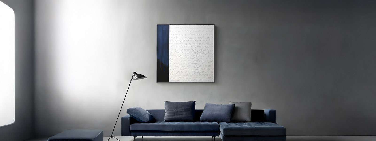 Large abstract wall art with a dark blue vertical band beside a white textured surface with fine script-like marks, above a blue sectional sofa in a grey room.
