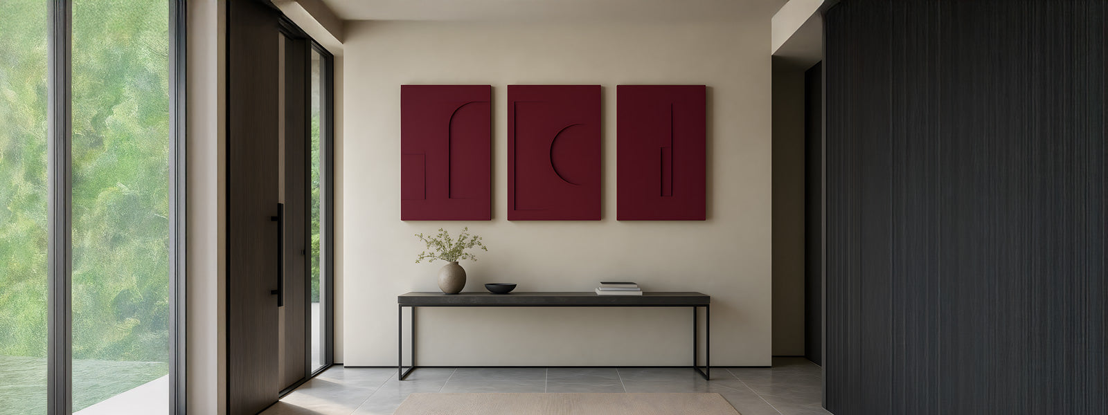 Three deep maroon relief wall art panels with minimal geometric forms above a slim dark console table in a modern hallway with tall windows.