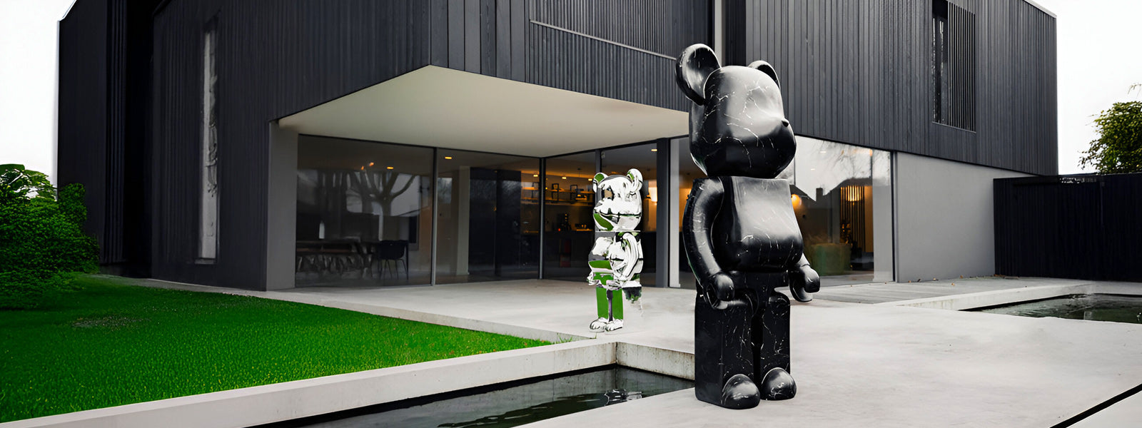 Two large bear sculptures in black marble-effect and reflective chrome with green accents on a concrete patio near a water feature outside a modern home.