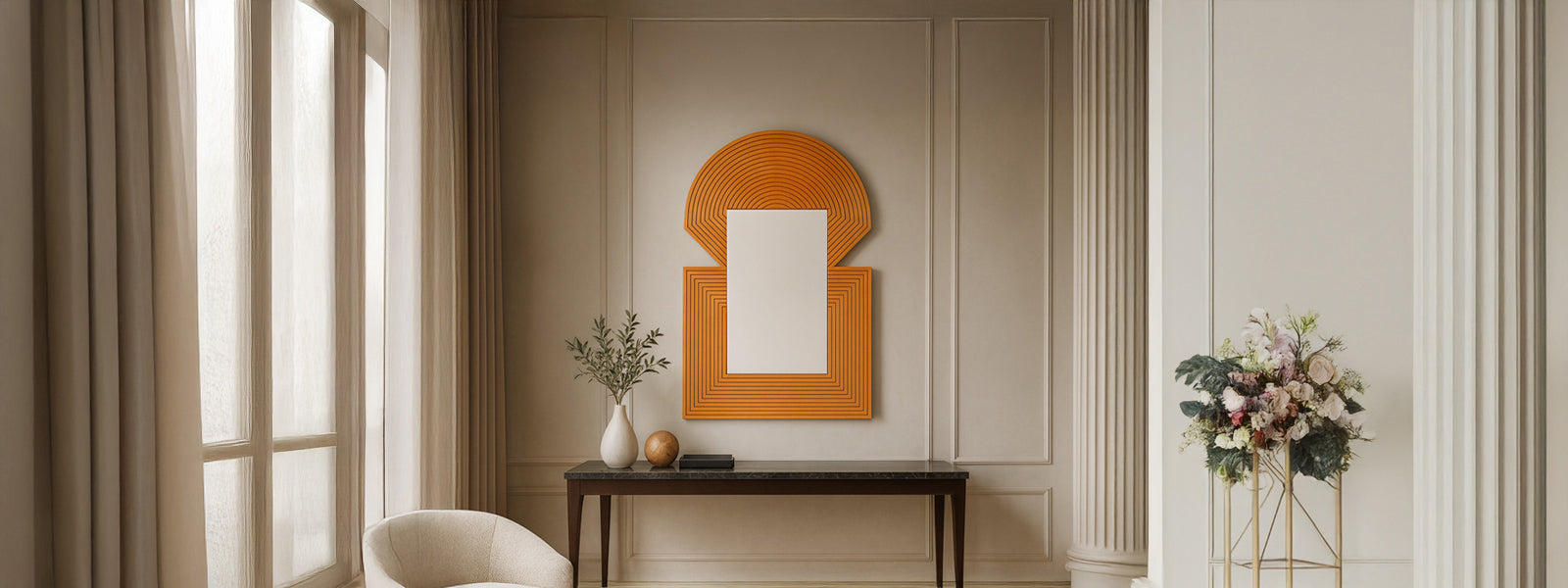 Orange arch-and-rectangle mirror art with concentric line patterns above a dark console table in a neutral paneled room with a white armchair and flowers.