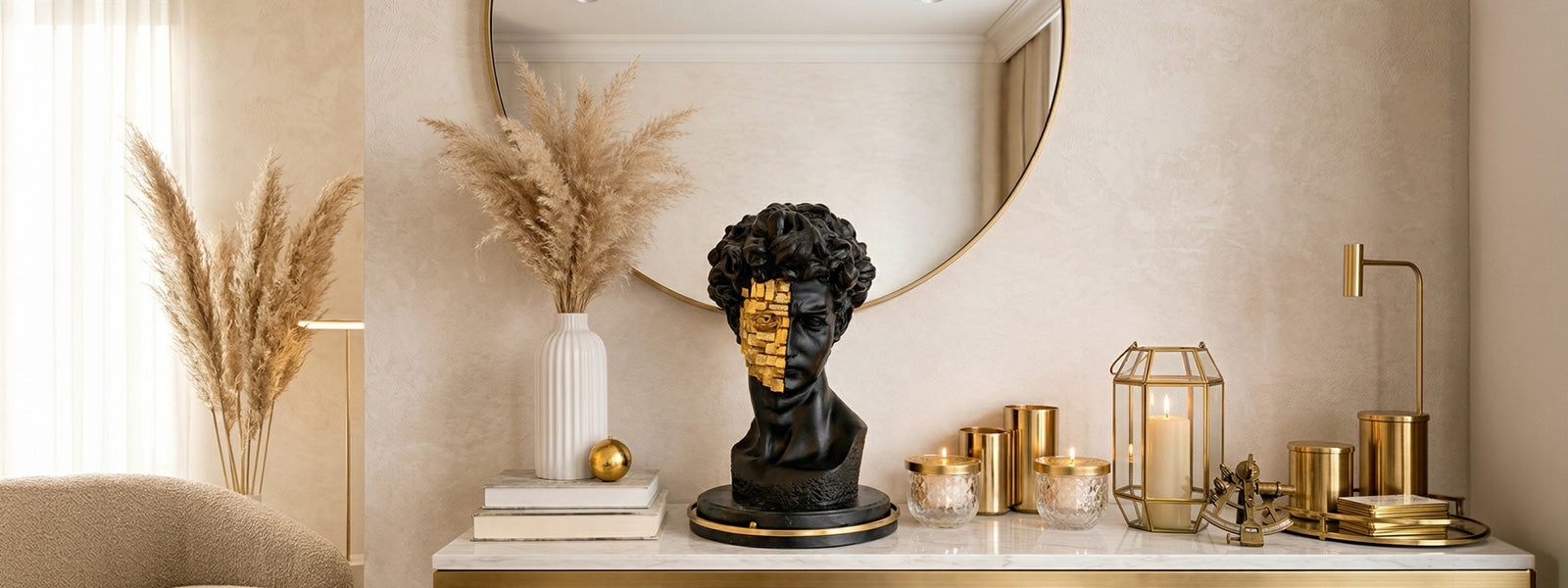 Black and gold resin David bust with mosaic gold leaf detail on a marble console beside pampas grass, candles, and gold accents in a neutral living room.