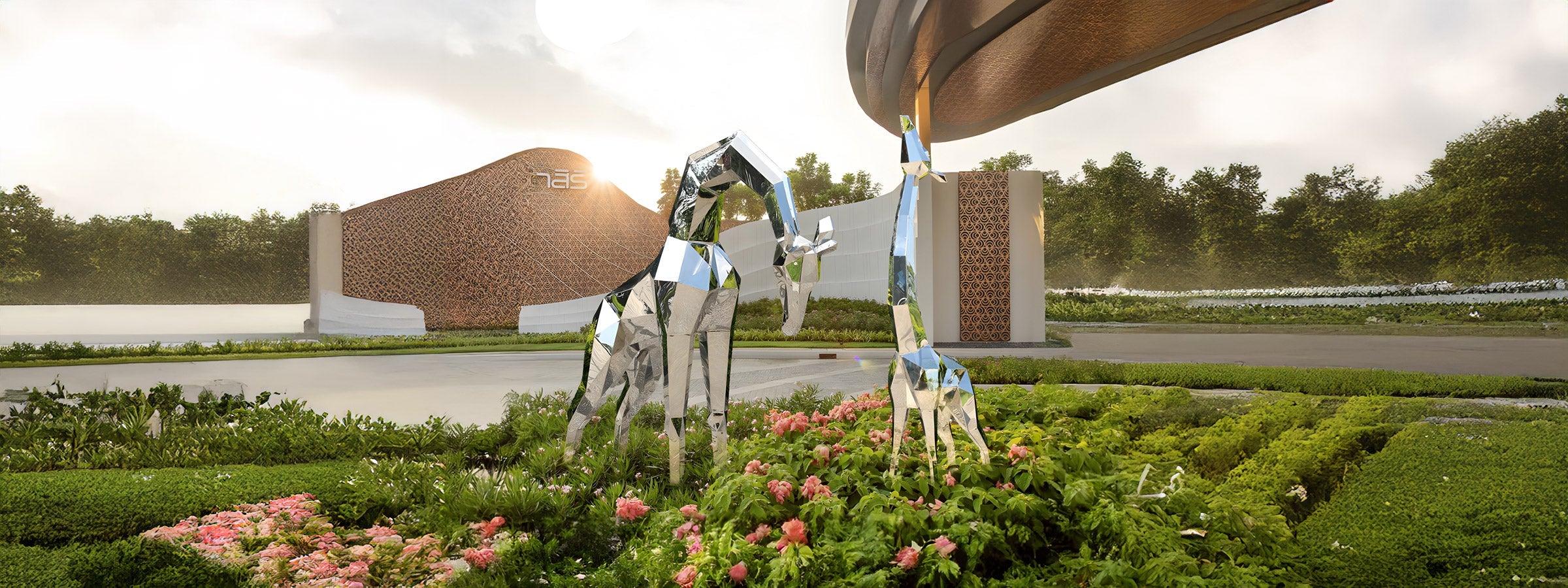 Mirror-polished stainless steel geometric giraffe sculptures, adult and juvenile, standing among pink flowers and lush greenery in a landscaped garden.