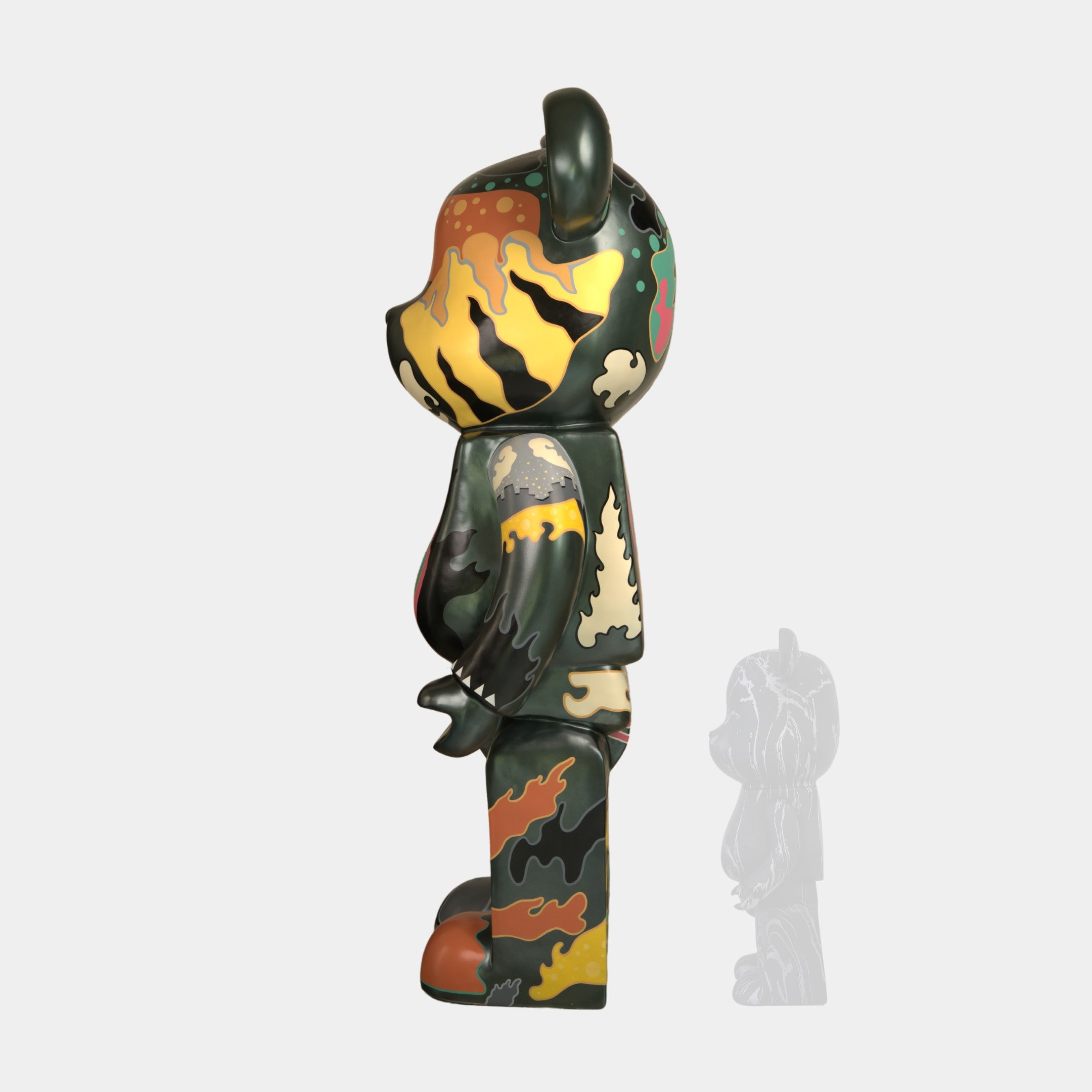The Inside Appears Outside Bear Sculpture - 50cm by Giant Sculptures features a side-profile bear in green, orange, yellow, and black camouflage. It stands upright on a light background with a smaller, semi-transparent version behind it.