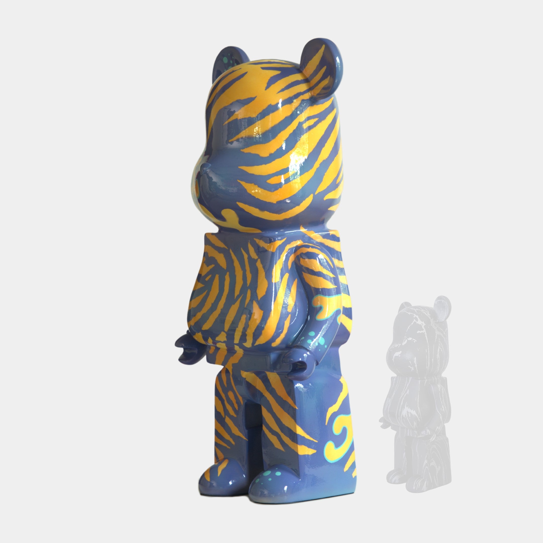 The Inside Appears Outside 2 Bear Sculpture (50cm) by Giant Sculptures features a blue body with bold yellow tiger stripes, standing upright. A smaller transparent version appears to its right, all set against a plain white background.