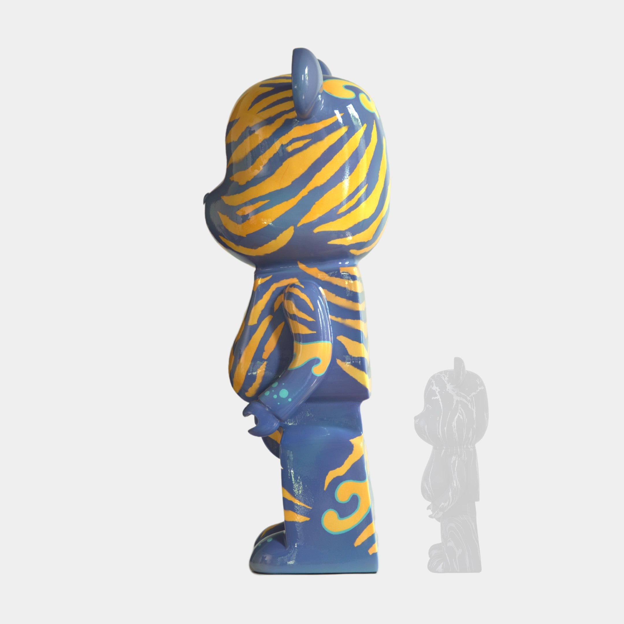 A blue bear-shaped figurine with yellow-orange tiger stripes stands in profile. This 50cm Inside Appears Outside 2 Bear Sculpture by Giant Sculptures is accompanied by a small translucent gray version on a plain white background.