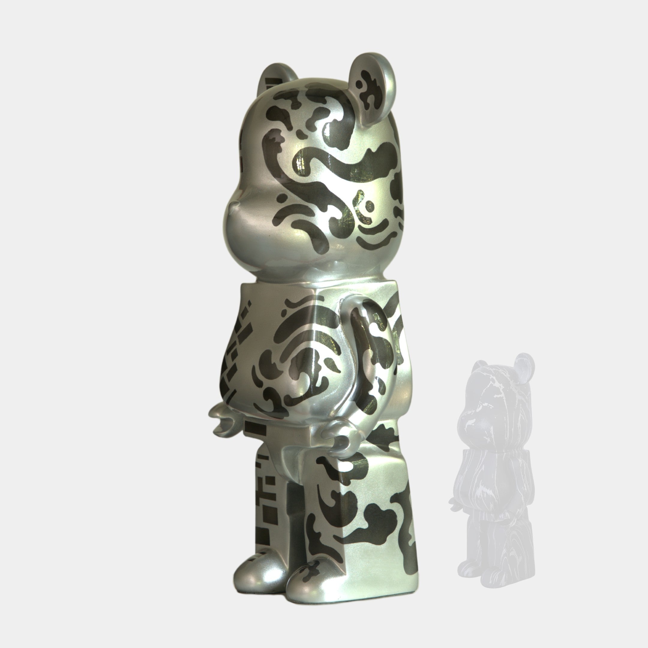 The Giant Sculptures Inside Appears Outside 3 Bear Sculpture (50cm) features a mirror-like silver bear with abstract black patterns, standing upright against a plain light gray background with its faint translucent reflection to the right.