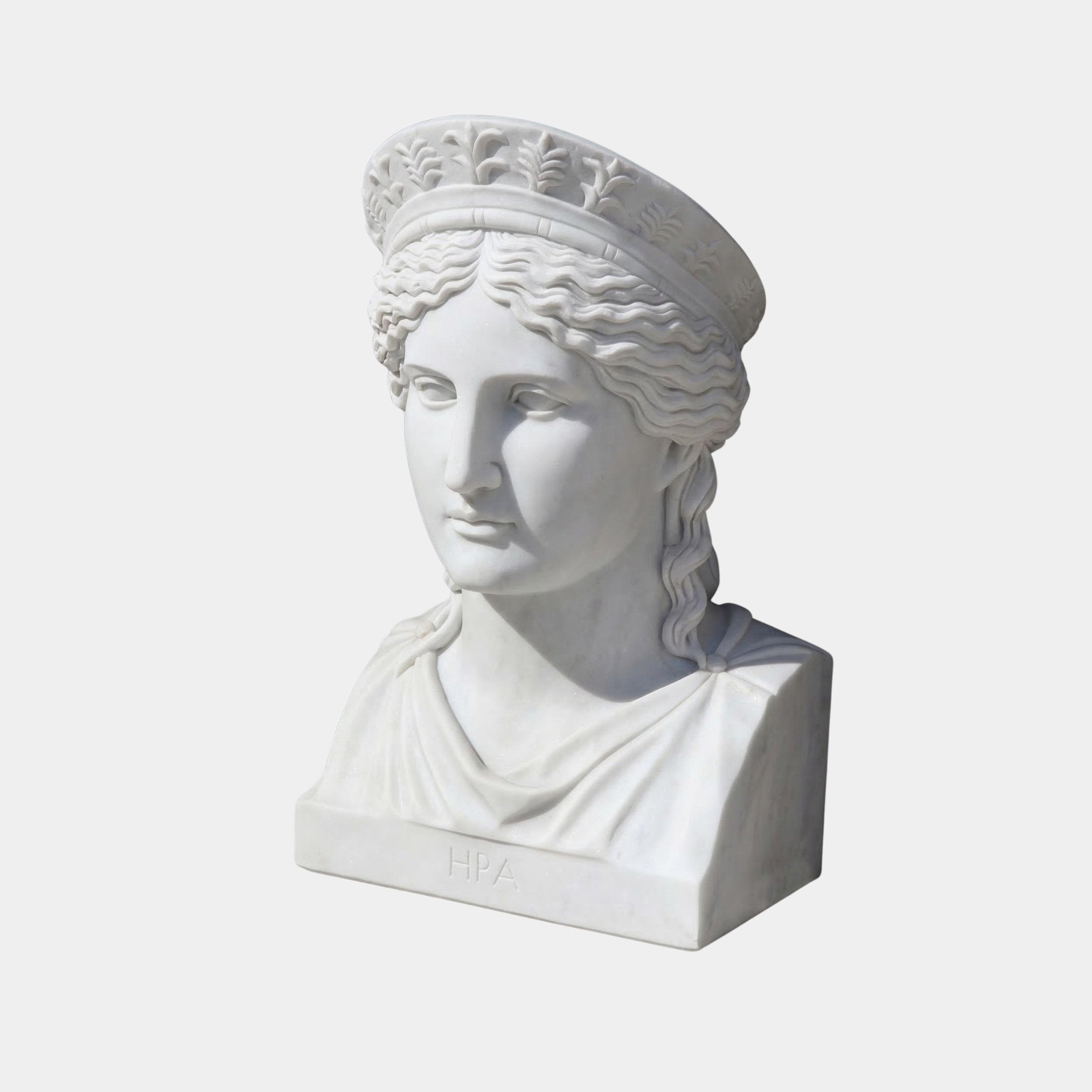 The Hera Marble Bust Sculpture by Giant Sculptures, measuring 50cm, depicts a woman with wavy hair, a classical headpiece, and draped clothing. The white marble piece has "HPA" inscribed at its base and is displayed against a plain white background.
