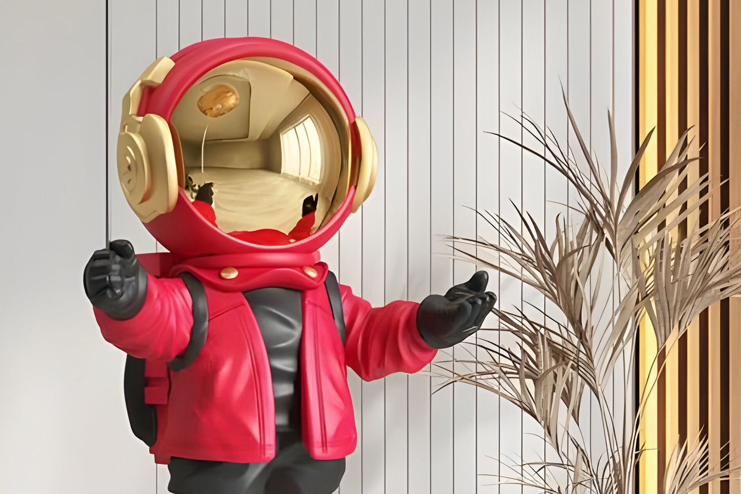 A small astronaut figurine with a shiny gold helmet is wearing a red jacket and black gloves. It stands with arms open in front of a background featuring vertical lines and decorative dried plants.