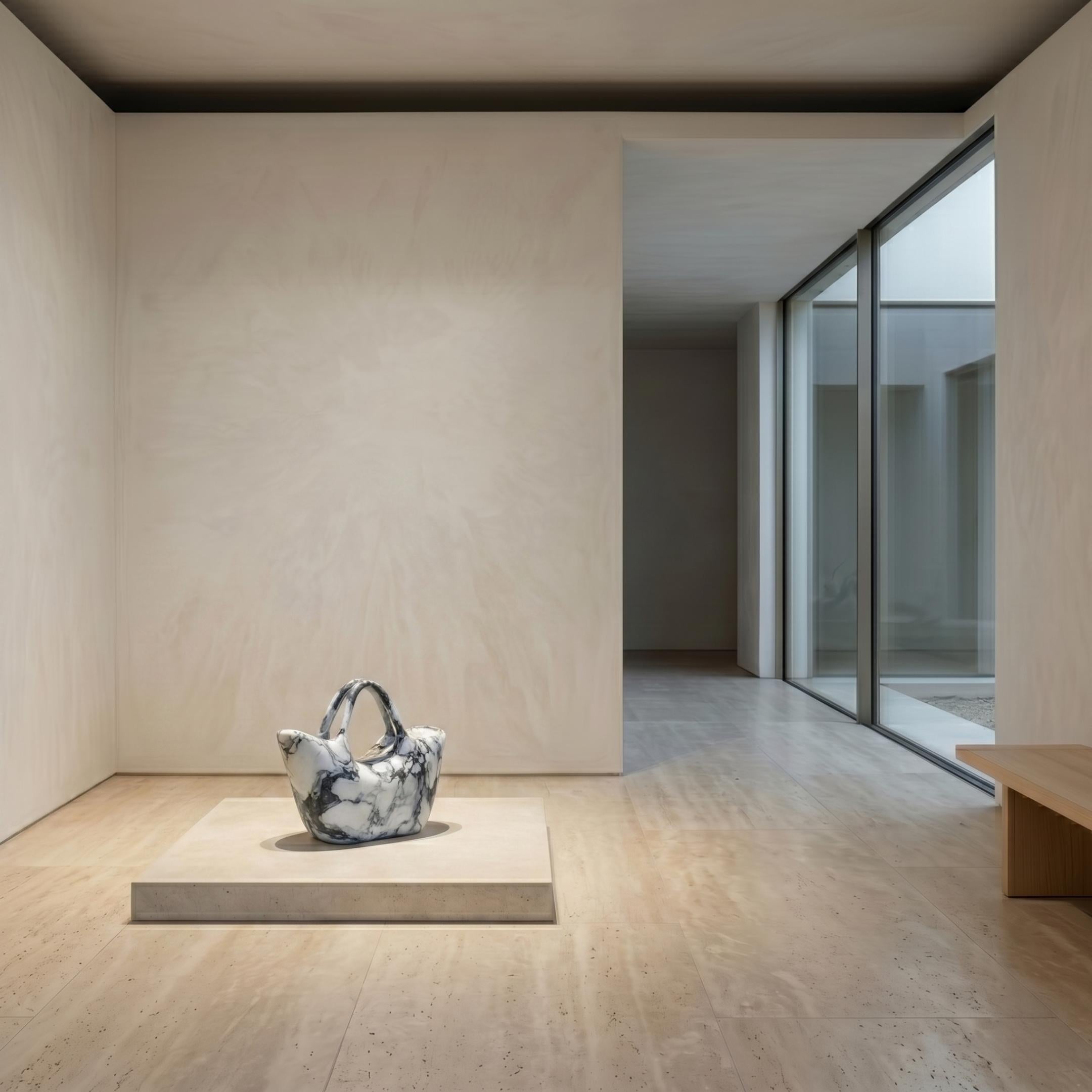 Bucket Bag Marble Sculpture 40cm by Giant Sculptures displayed on a low platform in a minimalist room with travertine floors and a courtyard view.