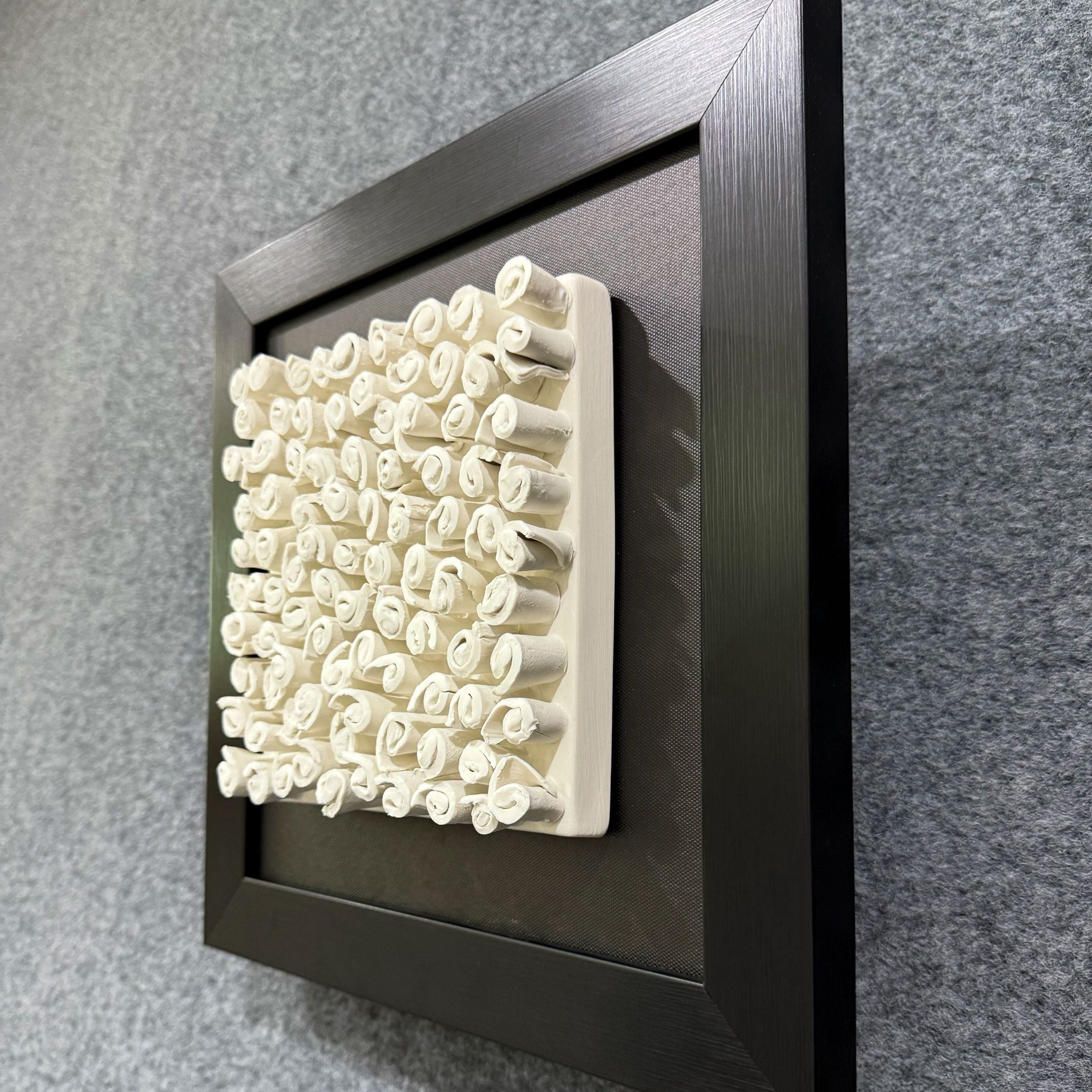The Harmonia 3D Spiral Wall Sculpture by Giant Sculptures features numerous upright white ceramic spirals on a rectangular base, framed in black—creating a striking textured effect ideal for modern spaces.