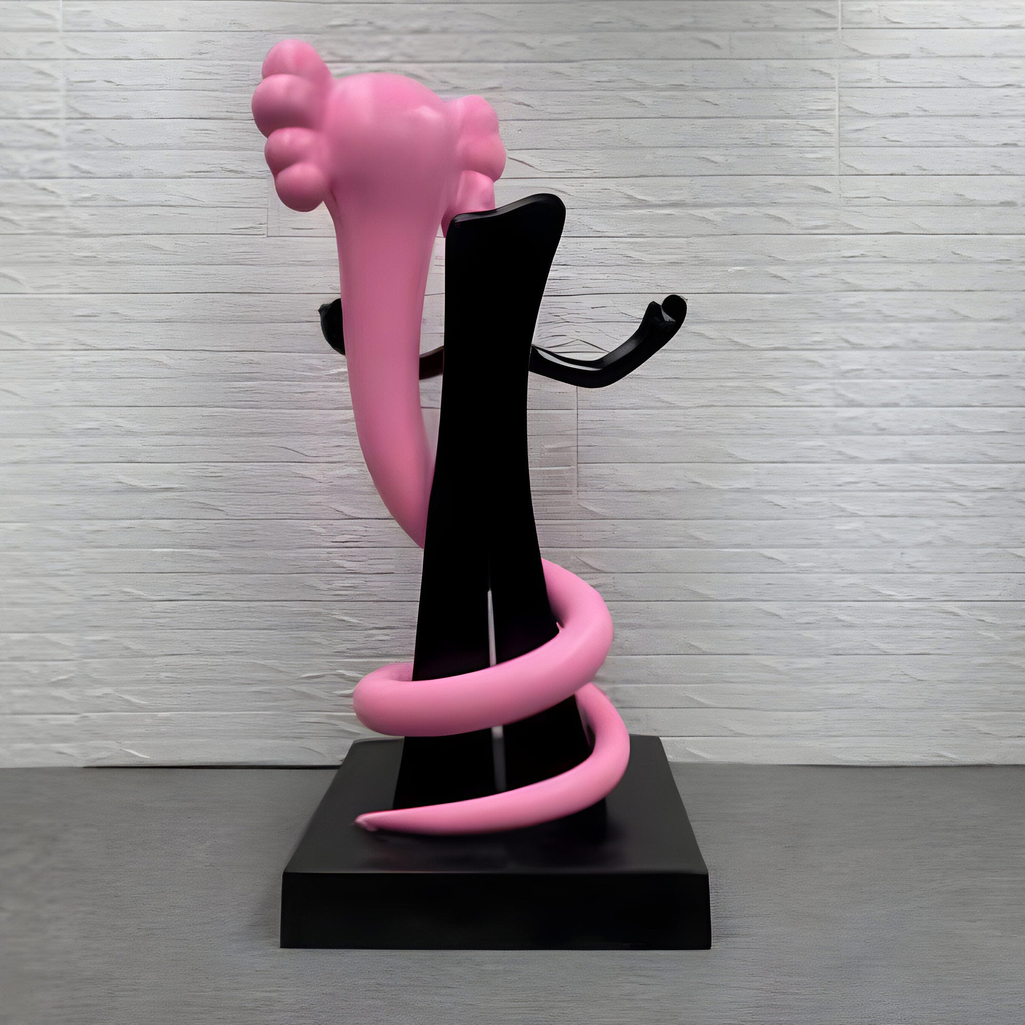 A black abstract sculpture elegantly interlocks with a pink, coiled form akin to the Giant Sculptures Petal Pink Iconify Snake Sculpture, 176 cm. Set against a textured white brick wall and smooth gray surface, it captures contemporary elegance and modern minimalism.