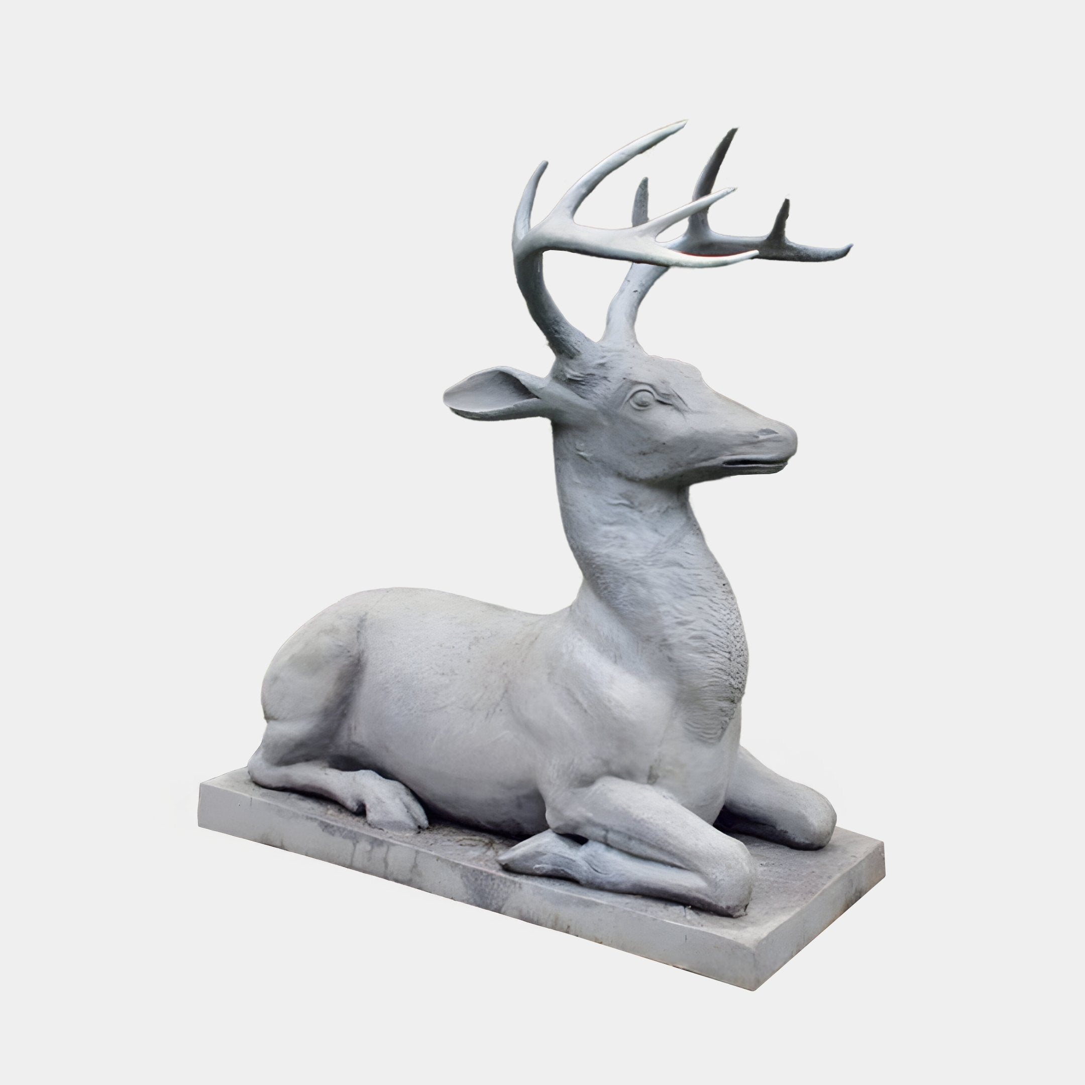 The Regal Lying Deer Marble Outdoor Sculpture by Giant Sculptures features a tranquil gray stag with large antlers, elegantly poised on a rectangular base. It embodies serenity with its legs tucked beneath and gaze slightly upward, perfect for outdoor settings against a plain white background.