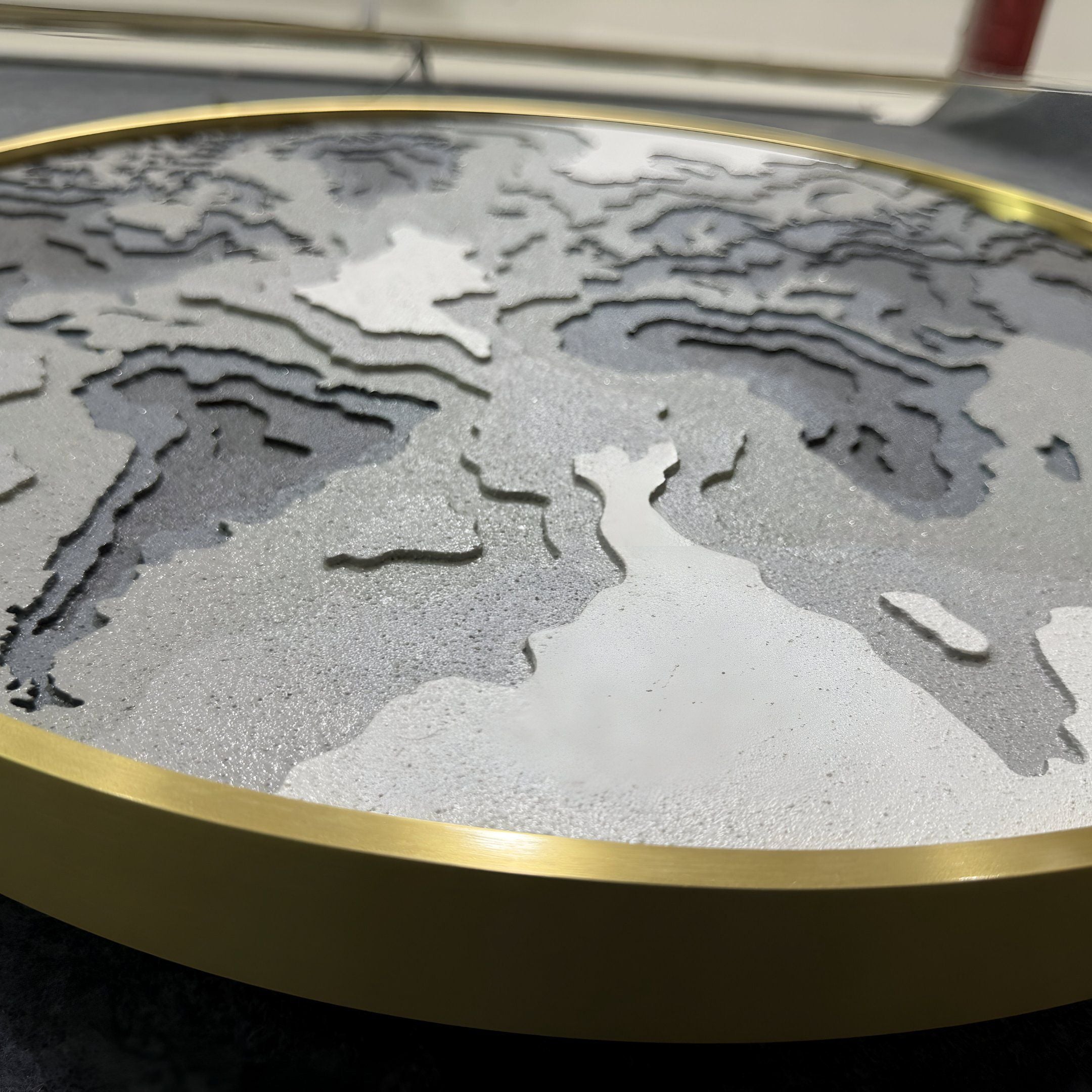The Terranova Earth Green Round Wood Carving 3D Wall Art by Giant Sculptures showcases textured gray and white surfaces with a metallic gold edge, depicting parts of Europe, Africa, and Asia in an elegant nature-inspired design.