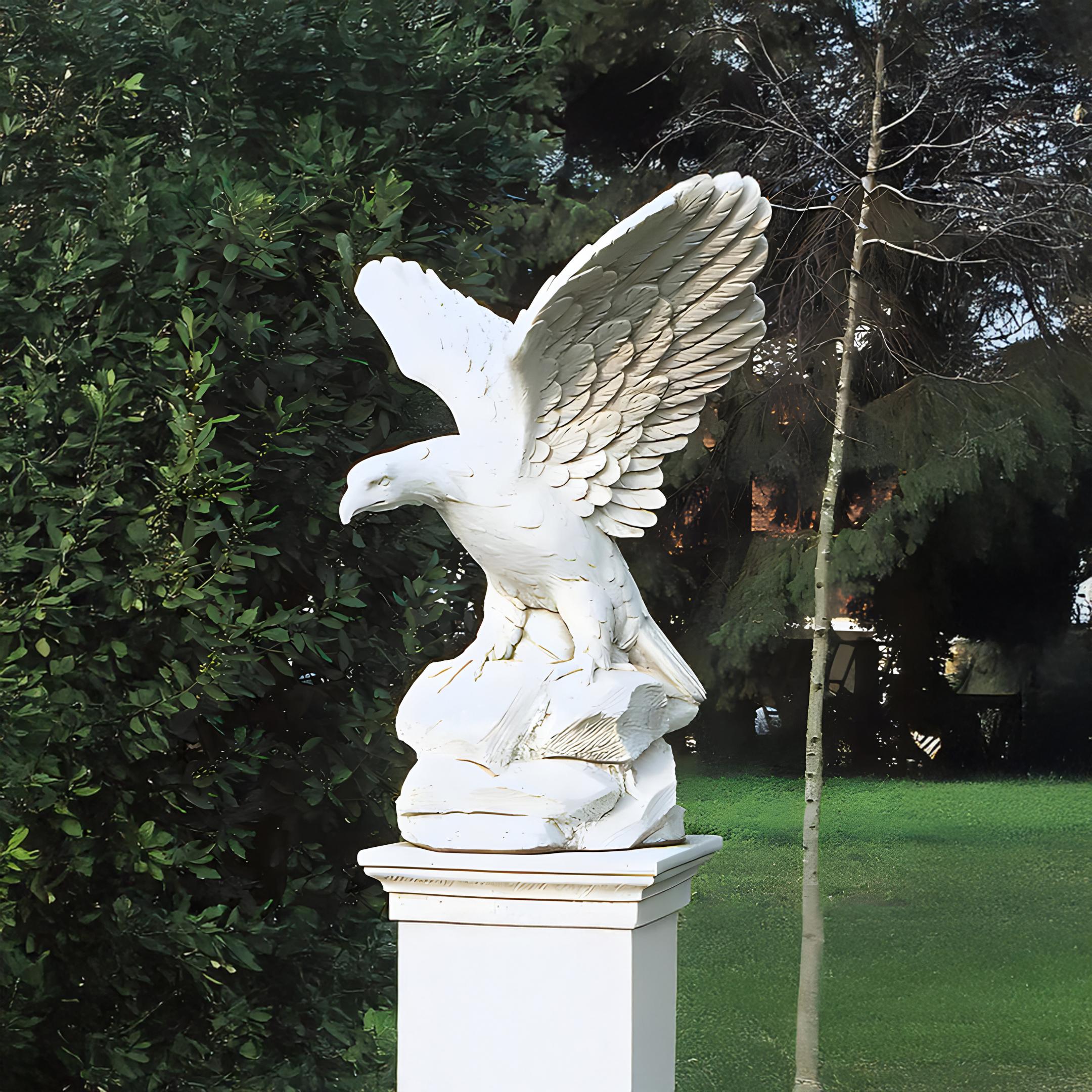 The Giant Sculptures Rock-Perched Eagle Marble Outdoor Sculpture (120cm) features a majestic white eagle with wings spread, elegantly placed on a rock against lush greenery and a small tree, enhancing the charm of any garden setting.