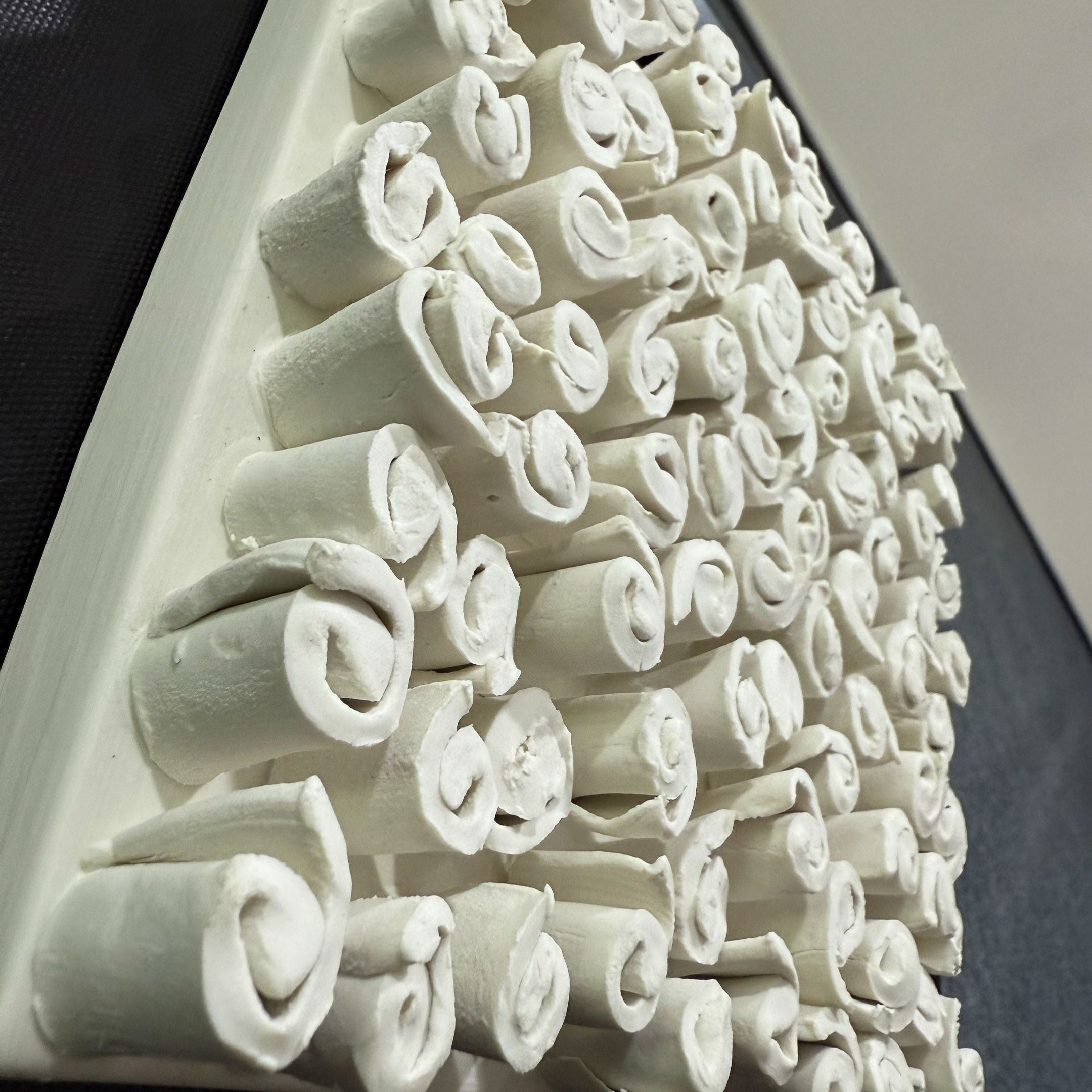 A close-up of white cylindrical forms, arranged in a neat pattern on an angled surface—ideal as the Harmonia 3D Spiral Wall Sculpture With Black Frame by Giant Sculptures, perfect for modern interiors. The background is blurred.