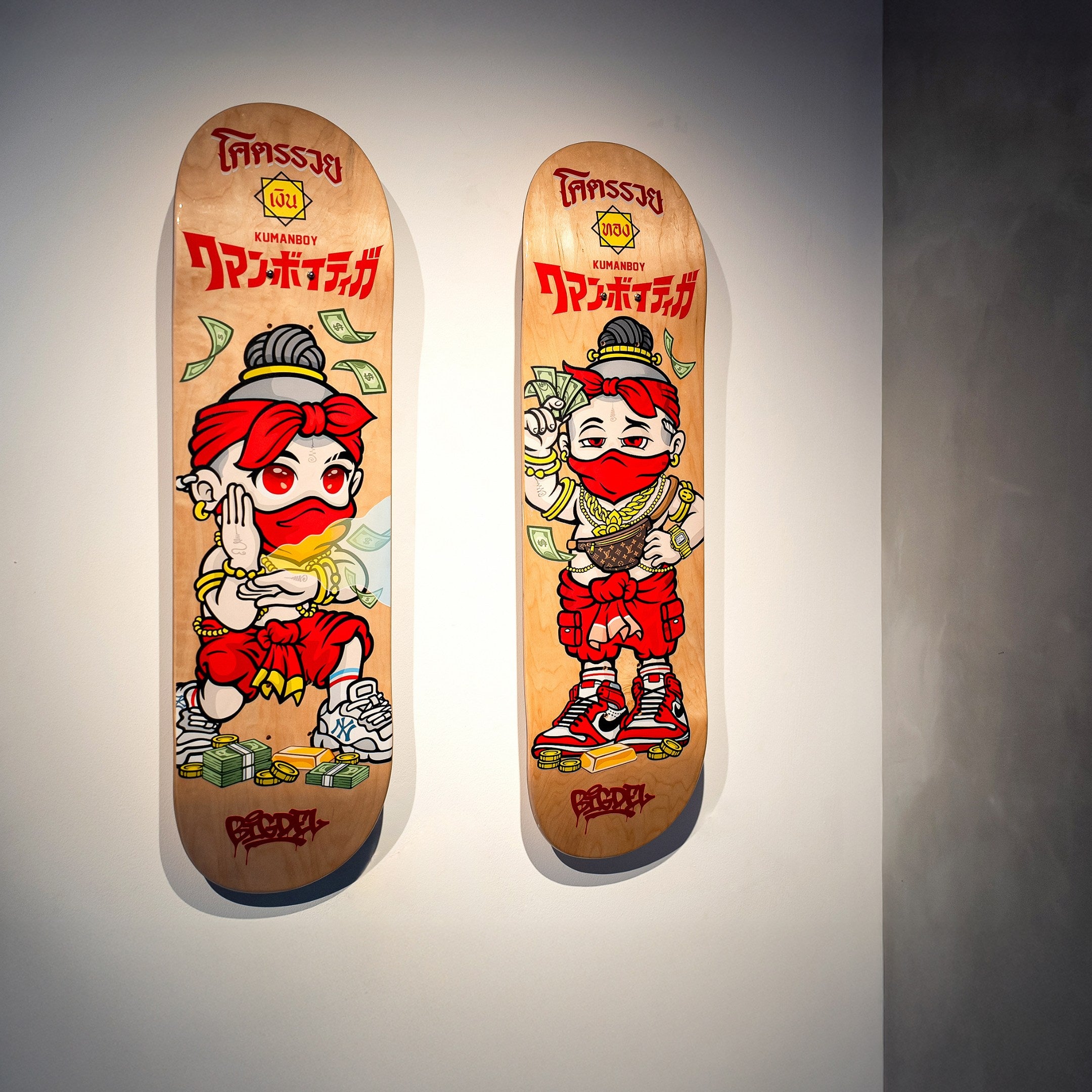 Two Kuman Boy Deck Vol.1 Skateboard Wall Art pieces by Giant Sculptures feature a red-masked cartoon character, stacks of money, and sneakers with bold retro-pop script in red and yellow, all mounted on the wall.