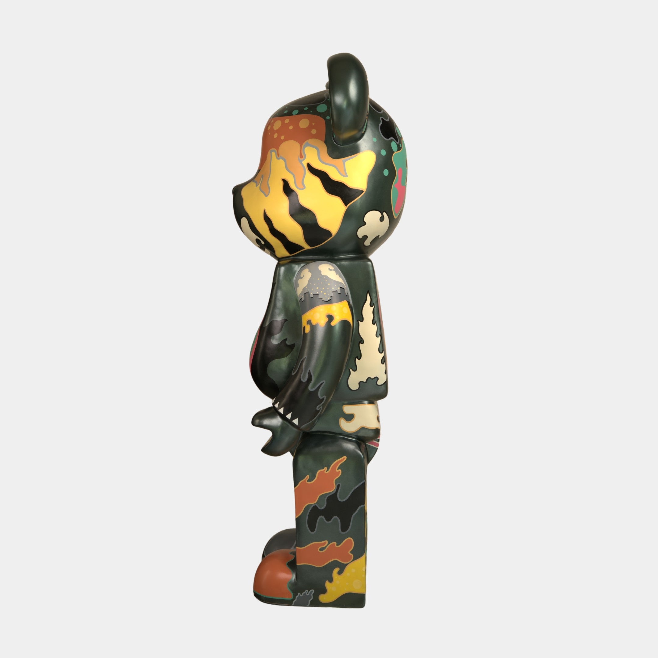 A side view of the 165cm Inside Appears Outside Bear Sculpture by Giant Sculptures, hand-painted in green, orange, yellow, and black camouflage, stands upright on a plain white background—an eye-catching piece inspired by Jirayu Tantrakul.