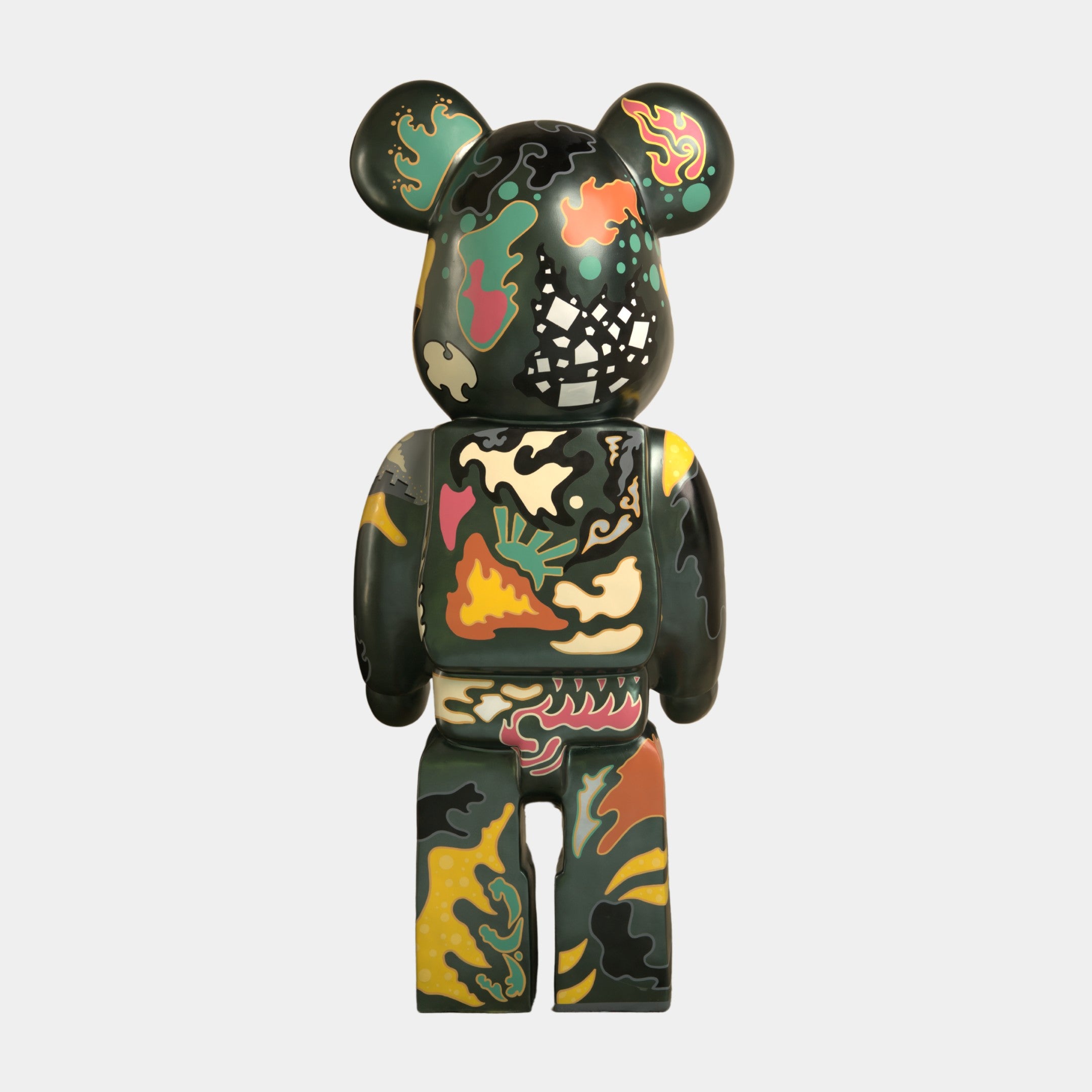The Inside Appears Outside Bear Sculpture - 165cm by Giant Sculptures features a hand-painted abstract camouflage in green, black, yellow, red, and beige. Viewed from the back, it has rounded ears and a blocky, toy-like body.