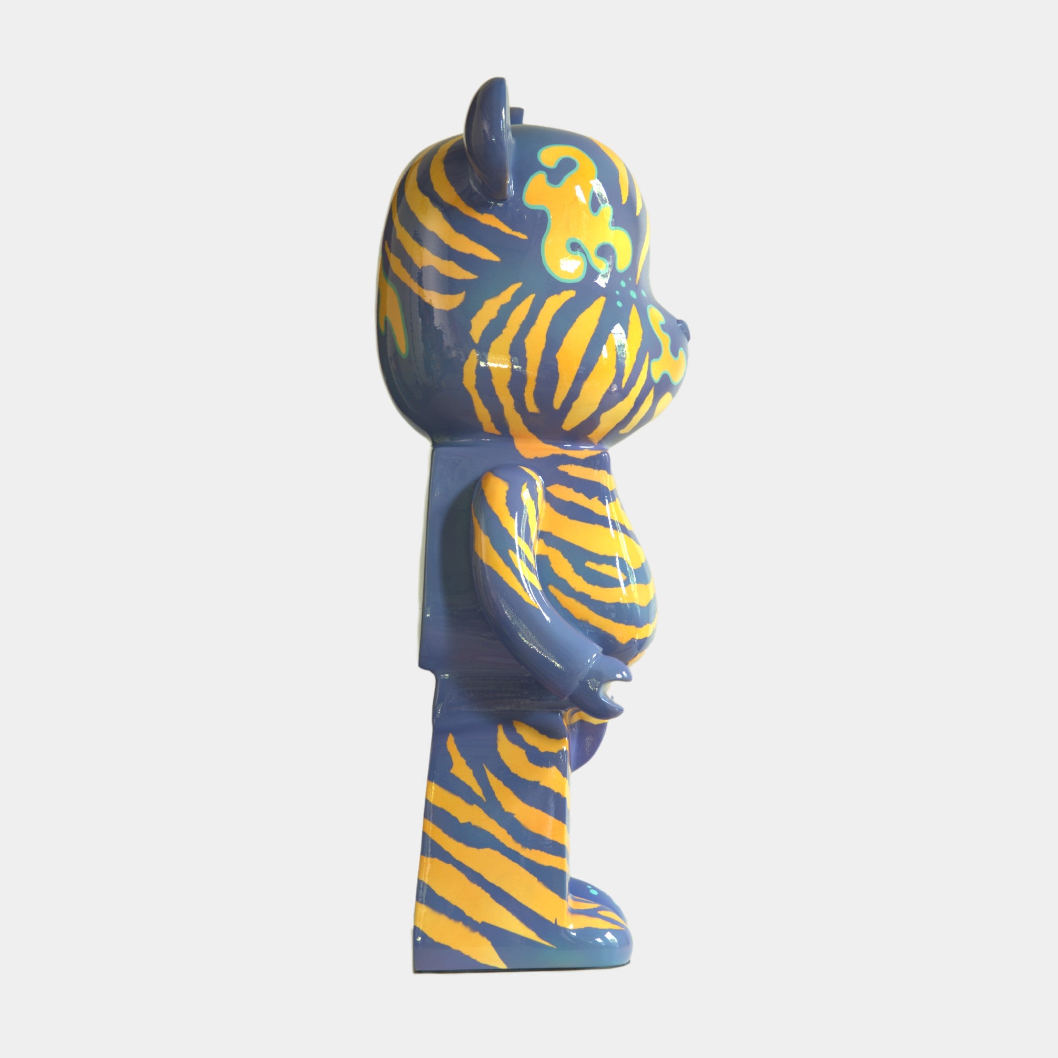 Side view of the Inside Appears Outside 2 Bear Sculpture - 135cm by Giant Sculptures, hand-painted with a blue base and bright yellow tiger stripes, standing upright against a plain white background.