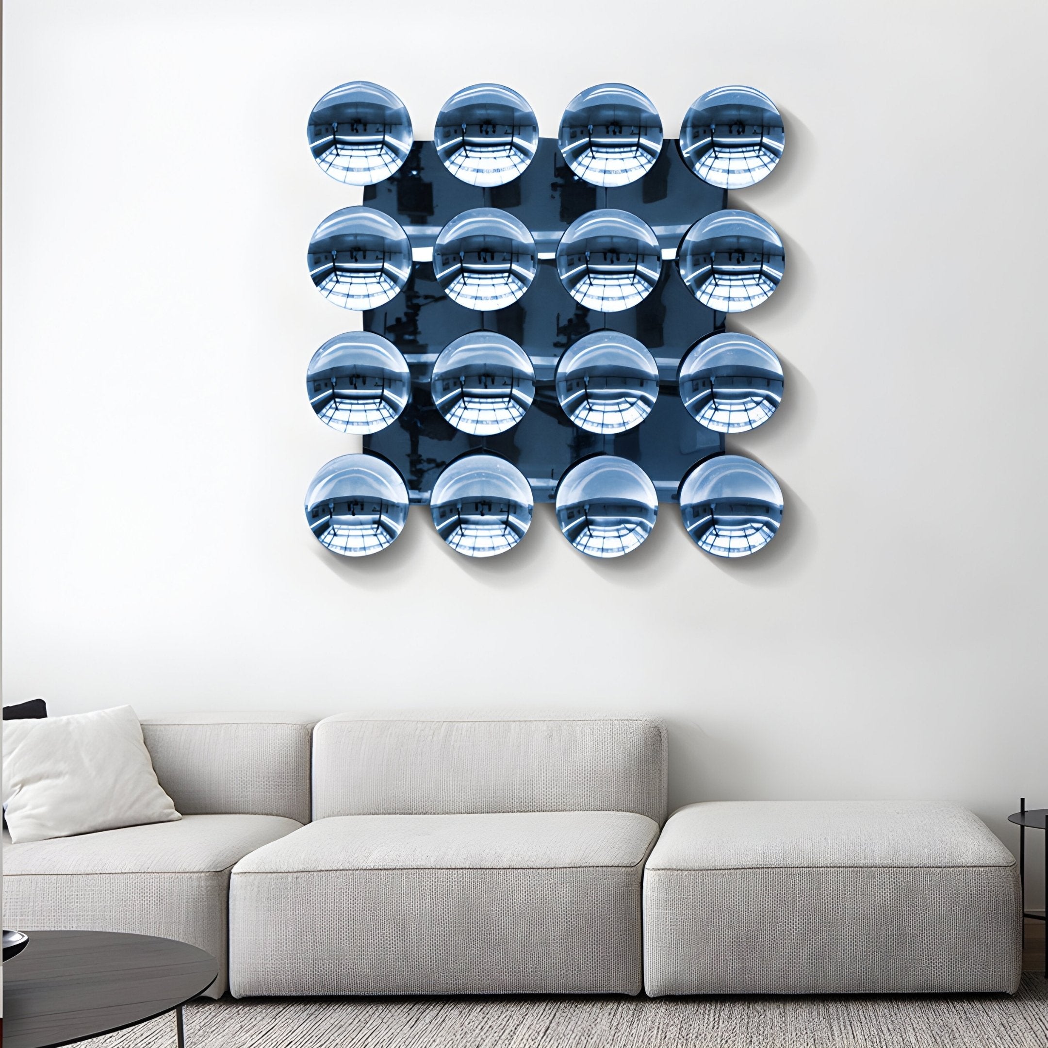 A modern living room with a white sectional sofa and the Giant Sculptures Dome Ice Blue Acrylic 3D Wall Art—16 reflective blue discs in a 4x4 grid—mounted above. A small round table sits to the right.