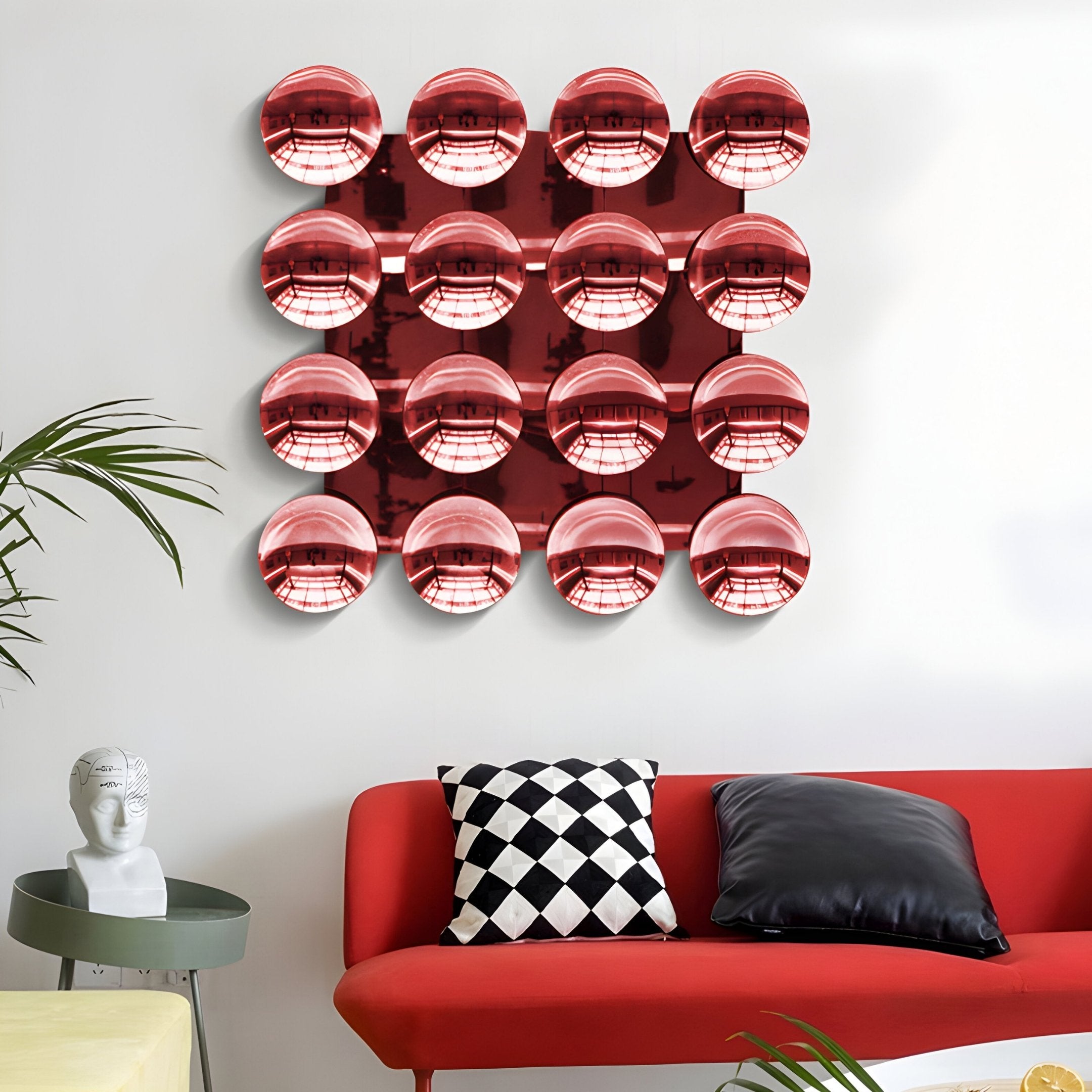 A modern living room with a red couch, black and white pillows, a decorative head sculpture, and the Giant Sculptures Dome Crimson Red Acrylic 3D Wall Art featuring 16 shiny crimson red spheres reflecting the room.