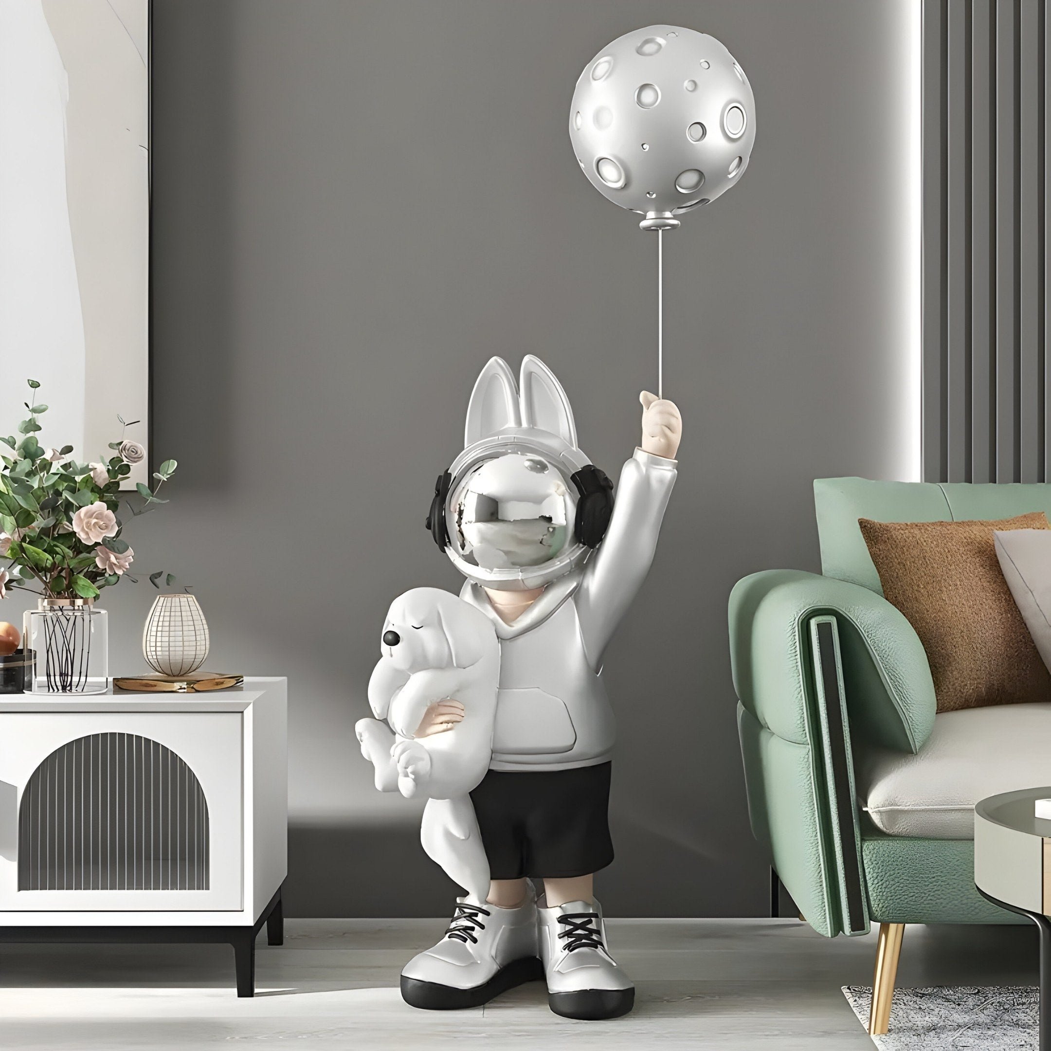 The Silver Astronaut Bunny Pup Balloon Sculpture from Giant Sculptures stands whimsically at 130cm in a modern living room, holding a bear and moon balloon. Its placed near a white console with plants and decor, close to a green sofa, creating an interstellar fantasy scene.