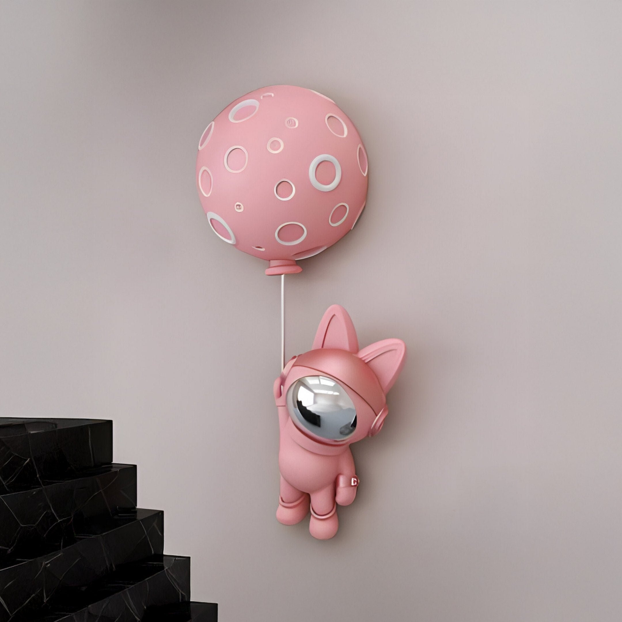 The Pink Astronaut Bunny Balloon 3D Wall Art (58cm) by Giant Sculptures, featuring a shiny pink bunny-eared astronaut, adds playful, futuristic charm to a plain wall near a black marble staircase.
