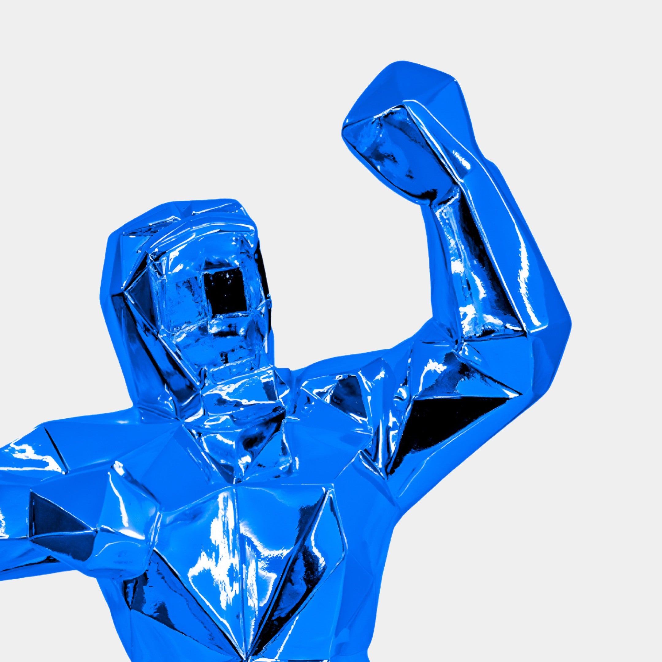 The Sapphire Blue Gorilla Sculpture - 165cm by Giant Sculptures features a shiny, electroplated finish and polygonal form with an arm raised in triumph. This indoor sculpture commands attention and admiration against a simple backdrop.