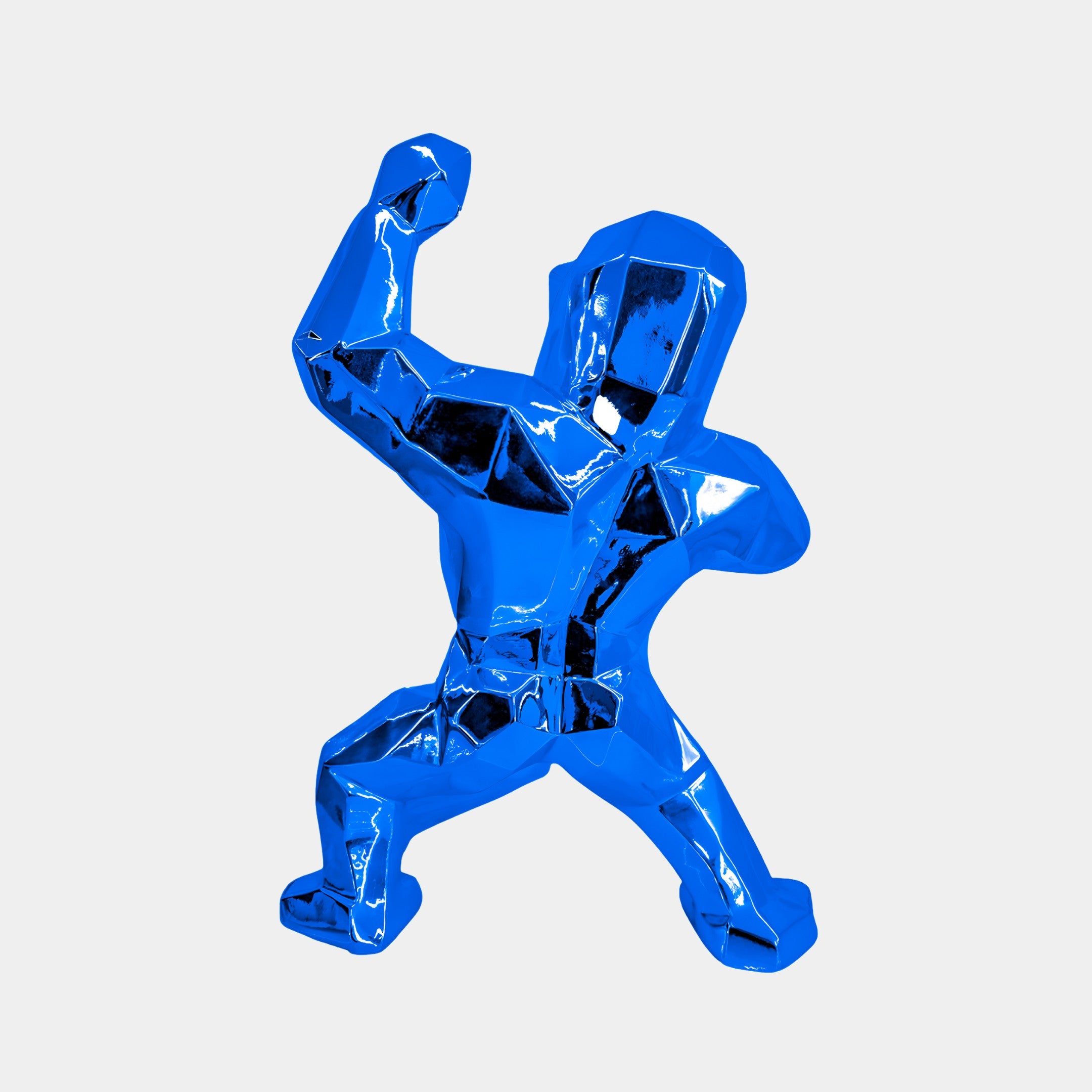 The Sapphire Blue Gorilla Sculpture - 50cm by Giant Sculptures features a shiny, faceted design, capturing a vibrant blue gorilla in an action pose with one arm raised and the other bent. Its surface reflects light beautifully against a simple light background, creating a striking contemporary piece.