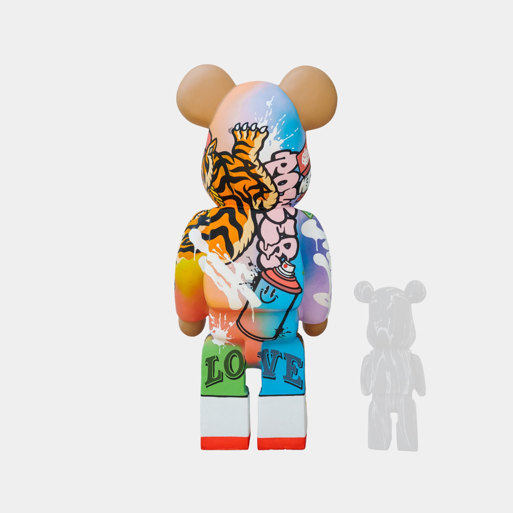 A vibrant bear-shaped figure with graffiti art features a tiger, spray paint, and the words Love and Forever. The design blends orange, blue, pink, and green hues. A smaller Lucky Paws Bear Sculpture by Giant Sculptures stands beside it for prosperity and protection.