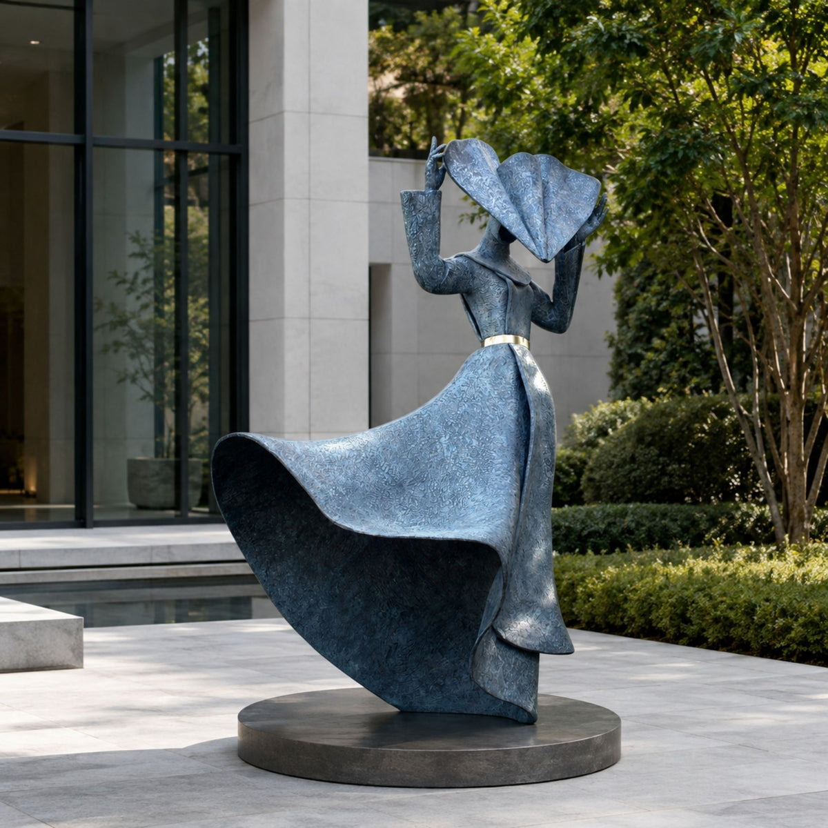 Large Contemporary Wind-Swept Female Figure Bronze Sculpture, 220cm, blue-toned patina on a round dark base, set on a courtyard patio near greenery and a modern building facade.