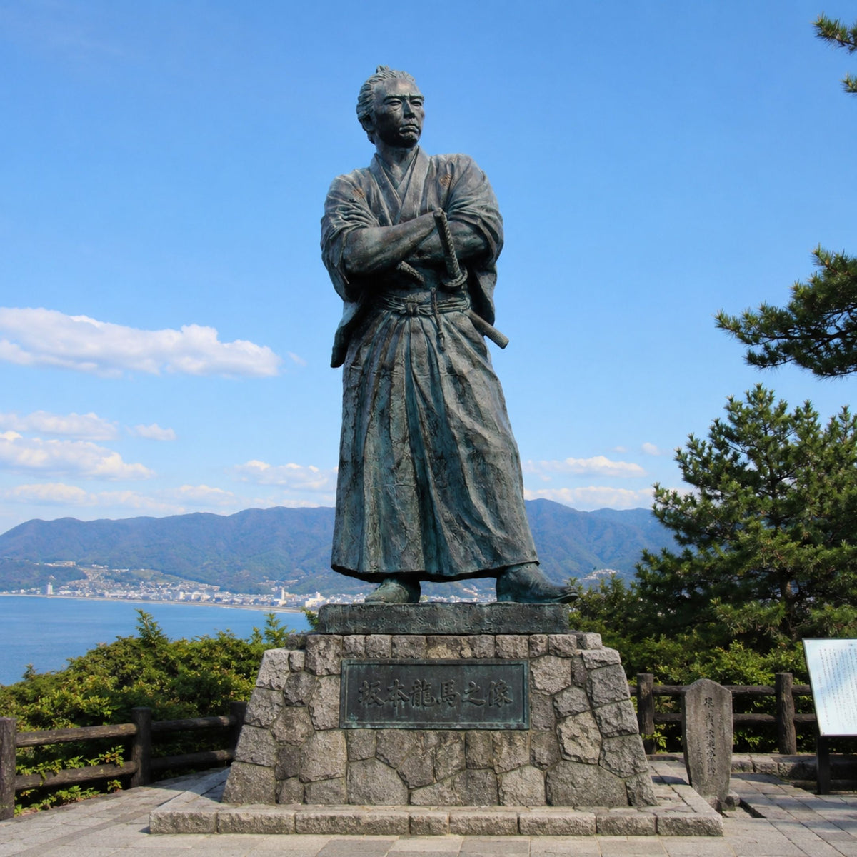 Monumental Traditional Samurai Warrior Bronze Sculpture - 350cm by Giant Sculptures, arms folded and katana at hip, standing on a stone pedestal overlooking a coastal mountain landscape.