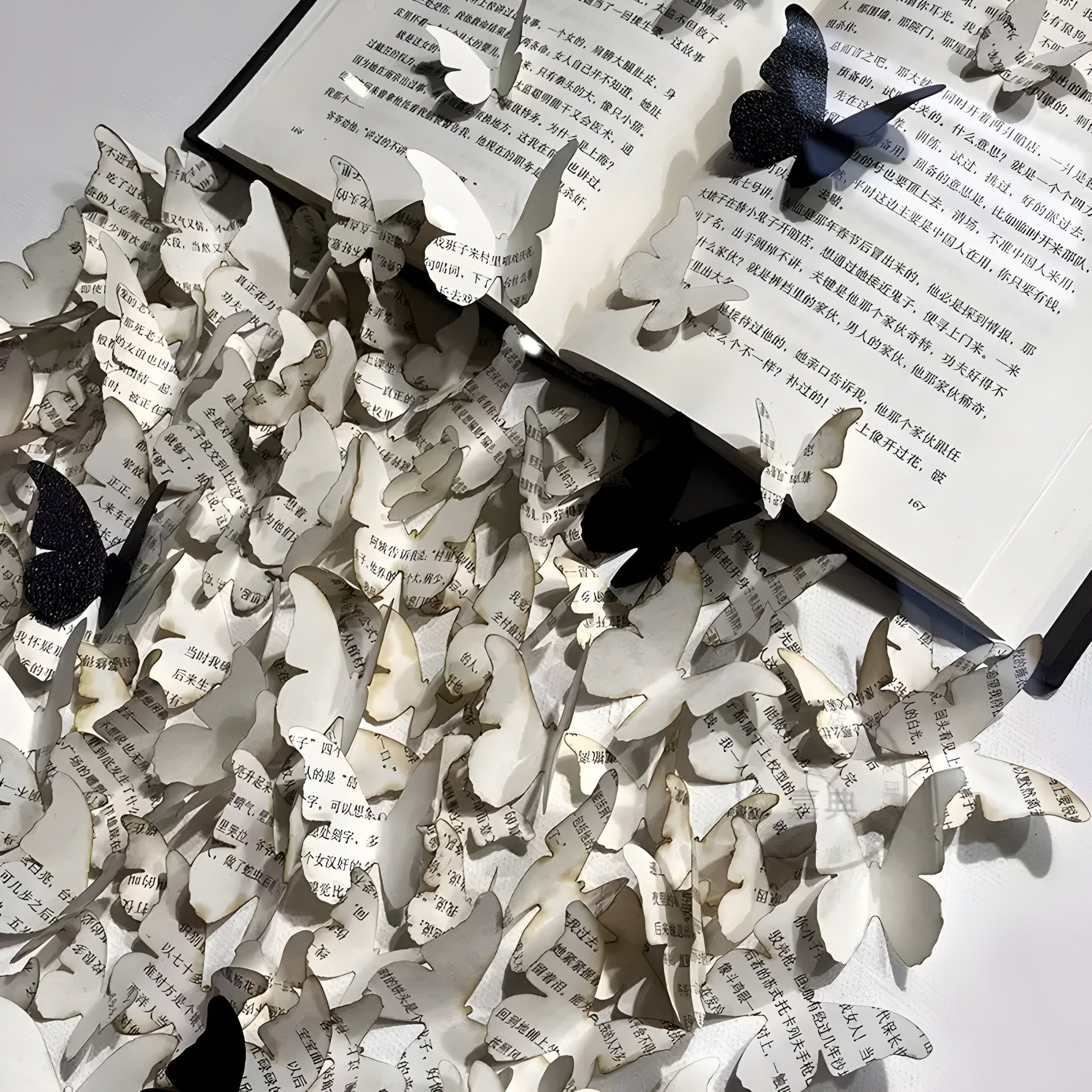 The Epiphany Black & White Butterfly Paper Wall Art by Giant Sculptures features an open book with pages transforming into butterfly shapes, creating a stunning 3D effect where primarily paper-colored and some black butterflies appear to emerge against a backdrop of Chinese text.