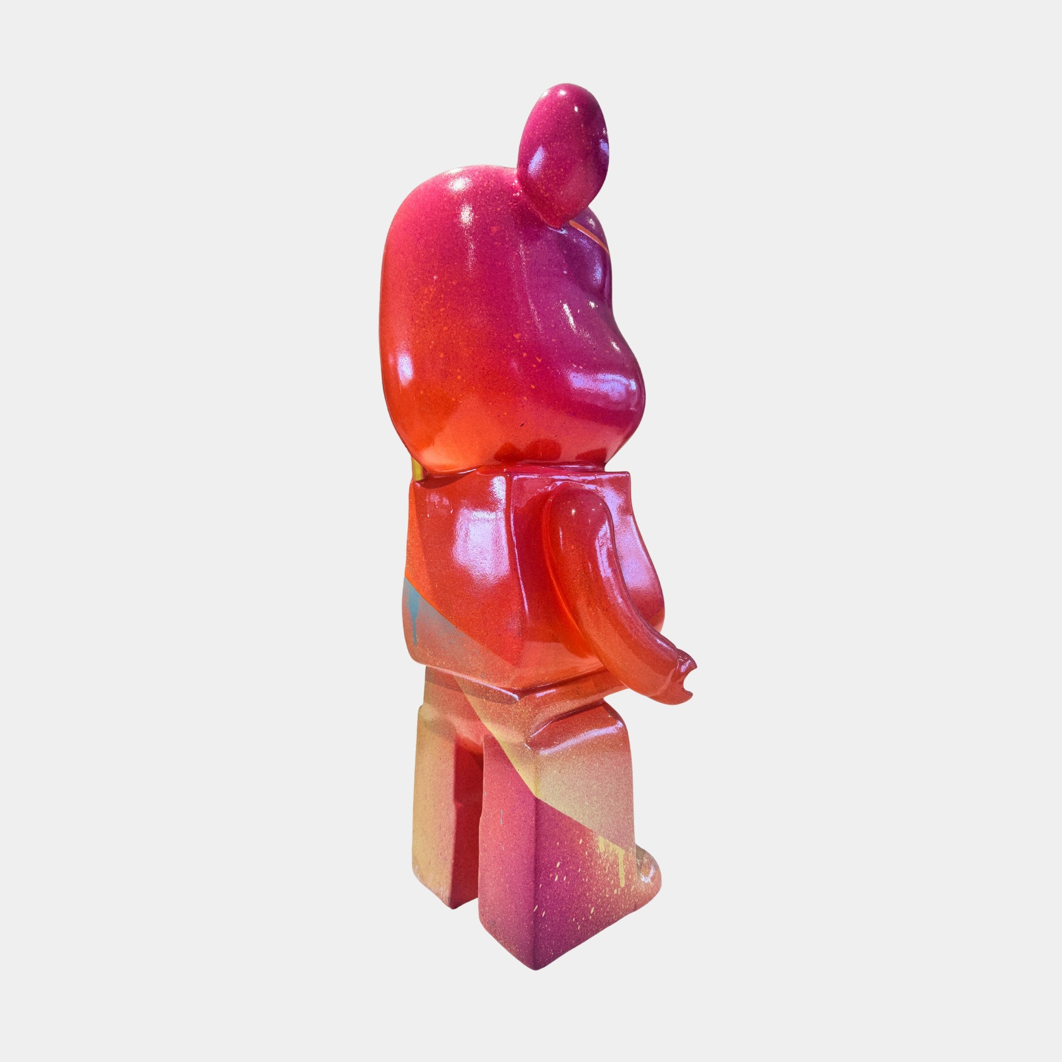 A glossy, bear-shaped toy figure from Giant Sculptures stands upright, viewed from behind, featuring a pink-red-yellow gradient. This limited edition Candy Bear Sculpture - 165cm resembles a work of contemporary art against a white background.