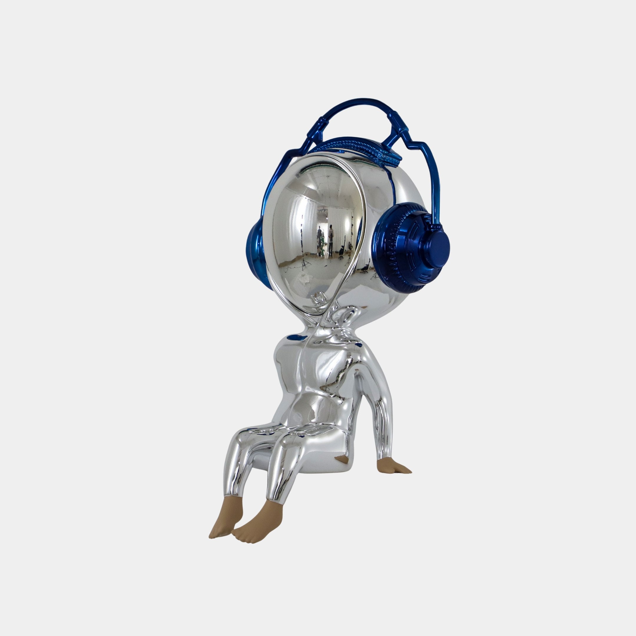 The Giant Sculptures Midnight Chrome Alien Beats Figure (55cm) features a shiny chrome finish, oversized mirrored helmet visor, large blue headphones, and sits barefoot against a white background—a striking futuristic decor piece.