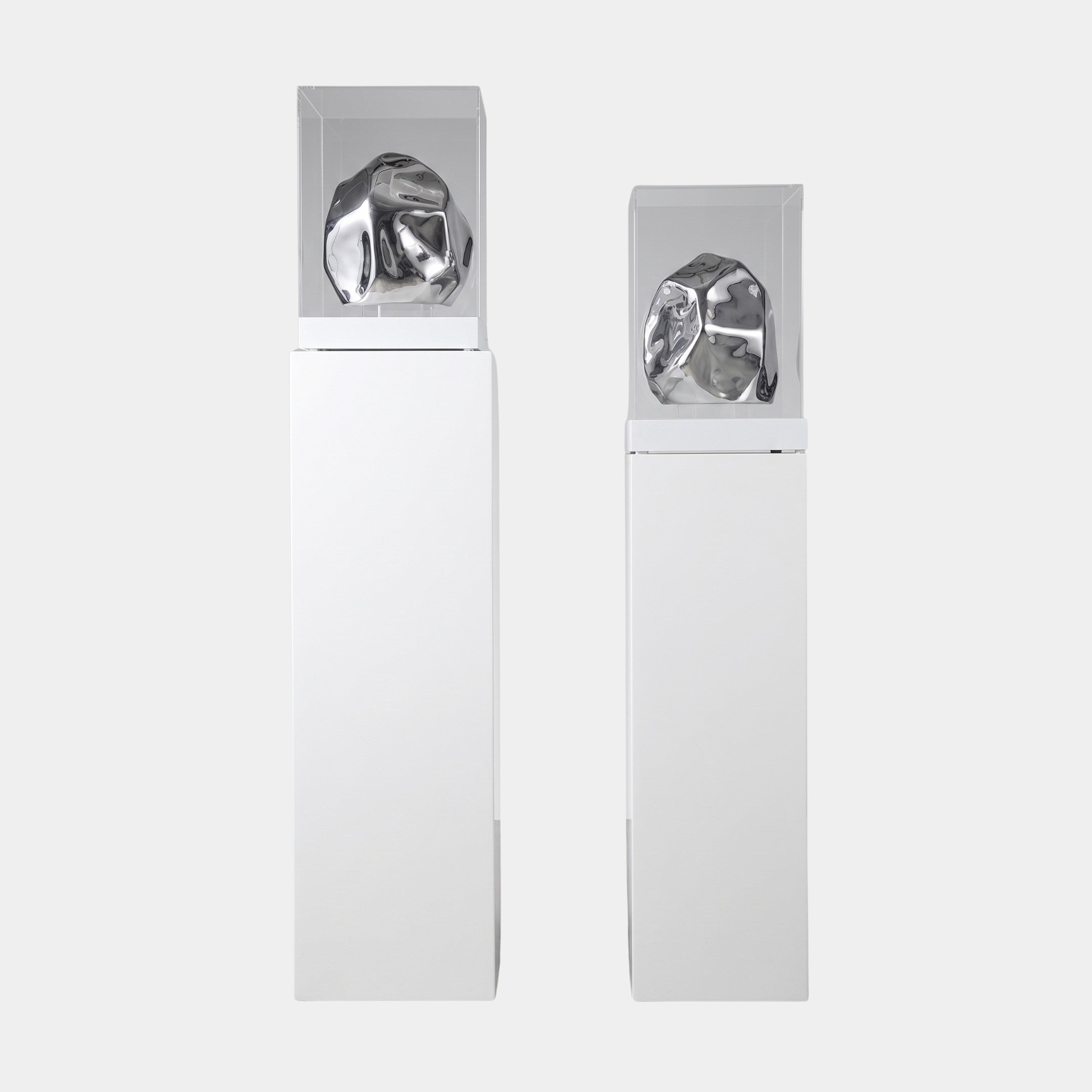 Pair of Giant Sculptures Silver Abstract Rock Display Sculptures in polished, faceted forms under clear cases atop tall white plinths against a plain background.