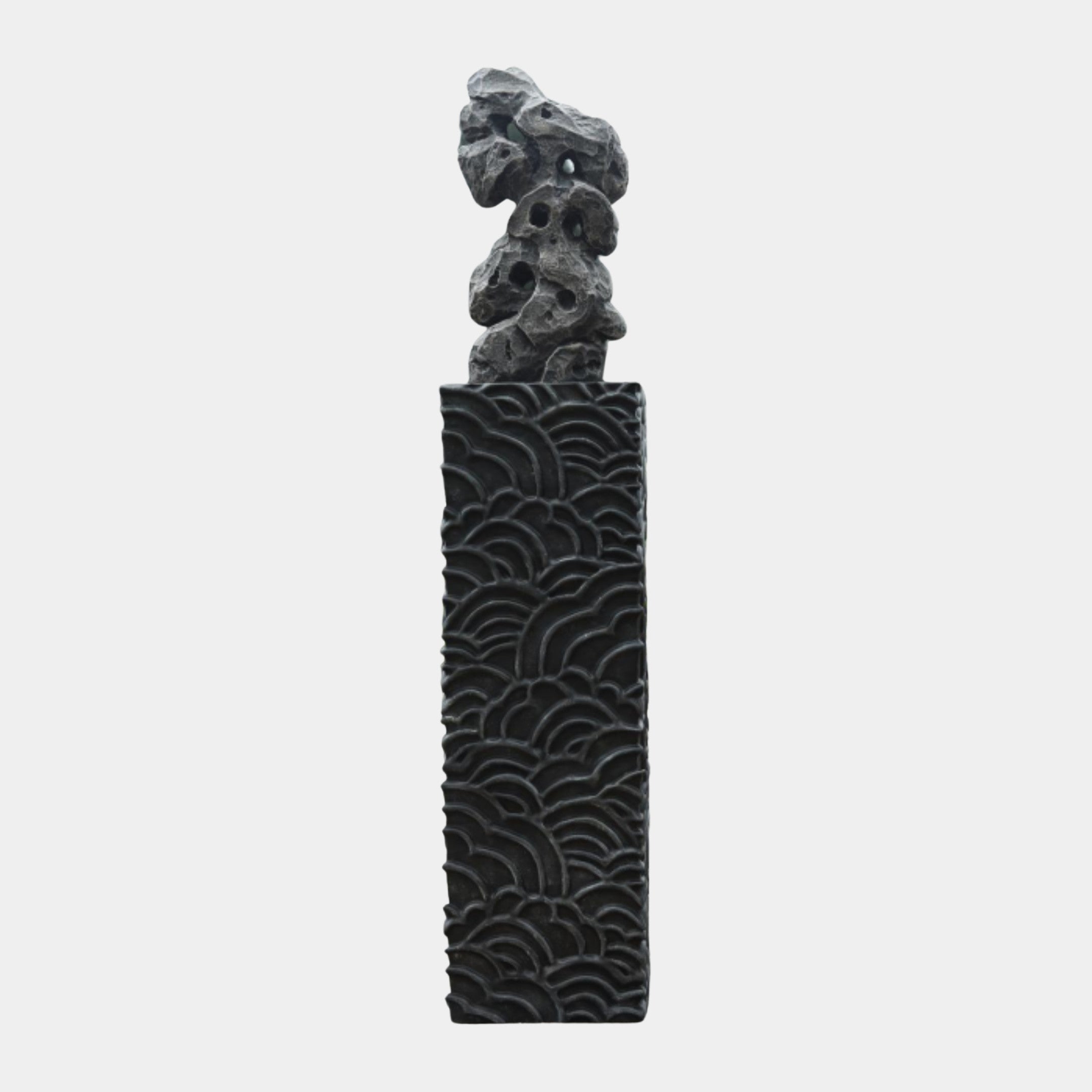Giant Sculptures' Black Abstract Crumbled Rock sculpture, a matte black porous scholar's rock atop a tall plinth carved with wave patterns, on a plain background.