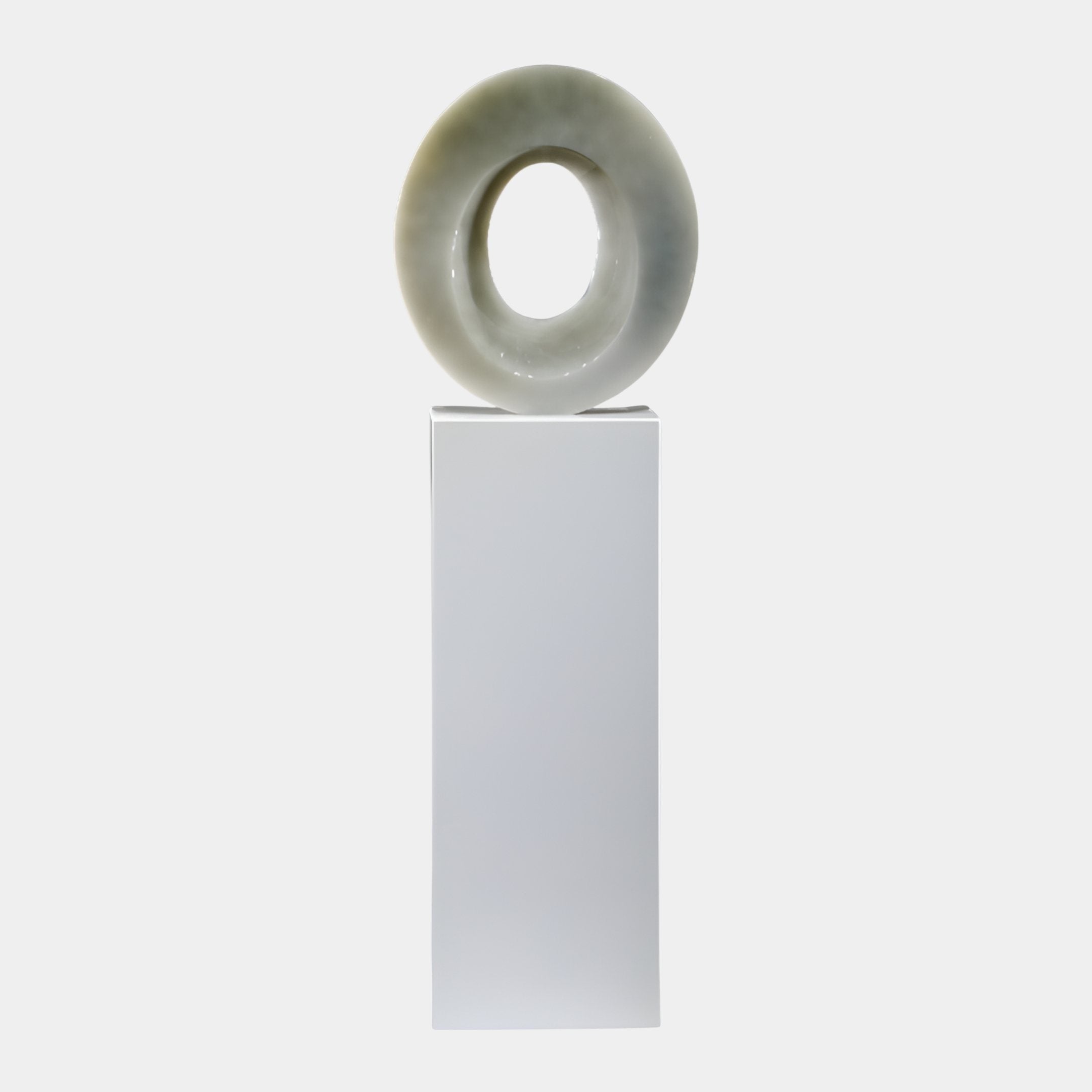 Zenith Ring Celadon Abstract Jade Sculpture by Giant Sculptures, a polished celadon-grey torus ring mounted on a tall white plinth against a plain background.