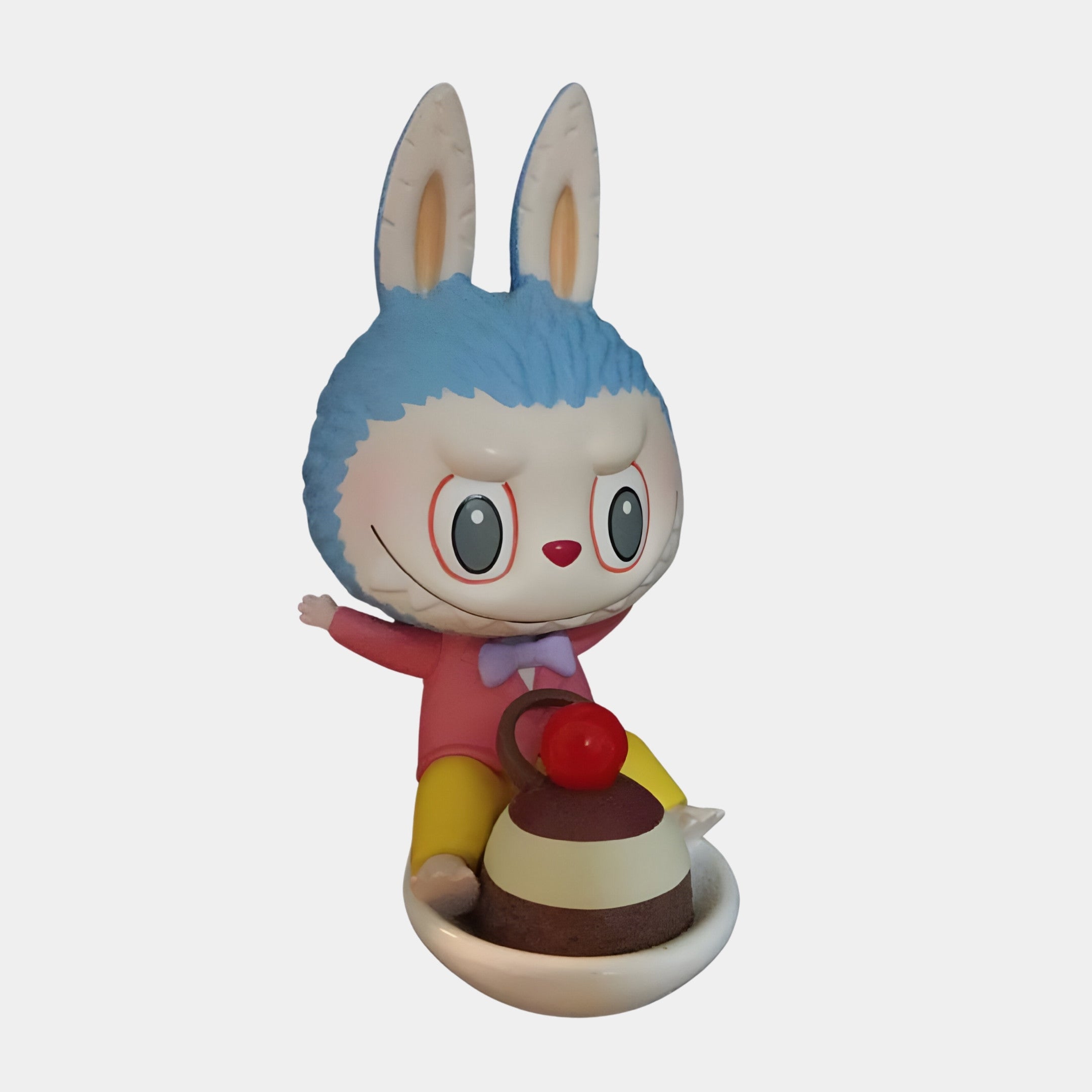 The Sweet Mischief Cherry Ride Labubu Sculpture (100cm) by Giant Sculptures features a blue-furred, big-eared rabbit with yellow pants, sitting on a white plate and holding a cherry-topped dessert—a delightful collectible.