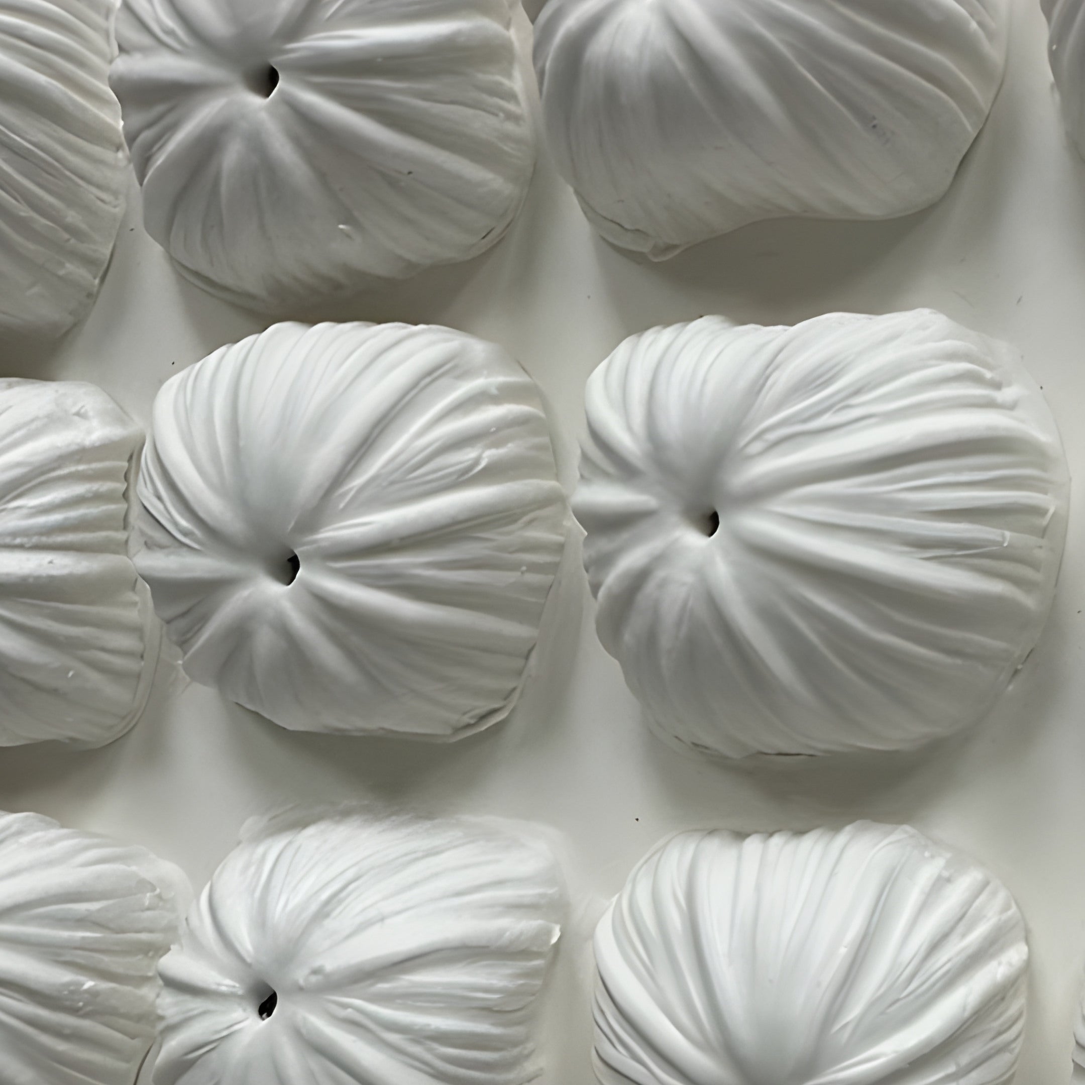 The Harmonia 3D Floral Grid Sculpture With Black Frame by Giant Sculptures features white, pillow-like shapes with pinched centers and textured surfaces, forming a floral-inspired pattern in a ceramic wall art arrangement.