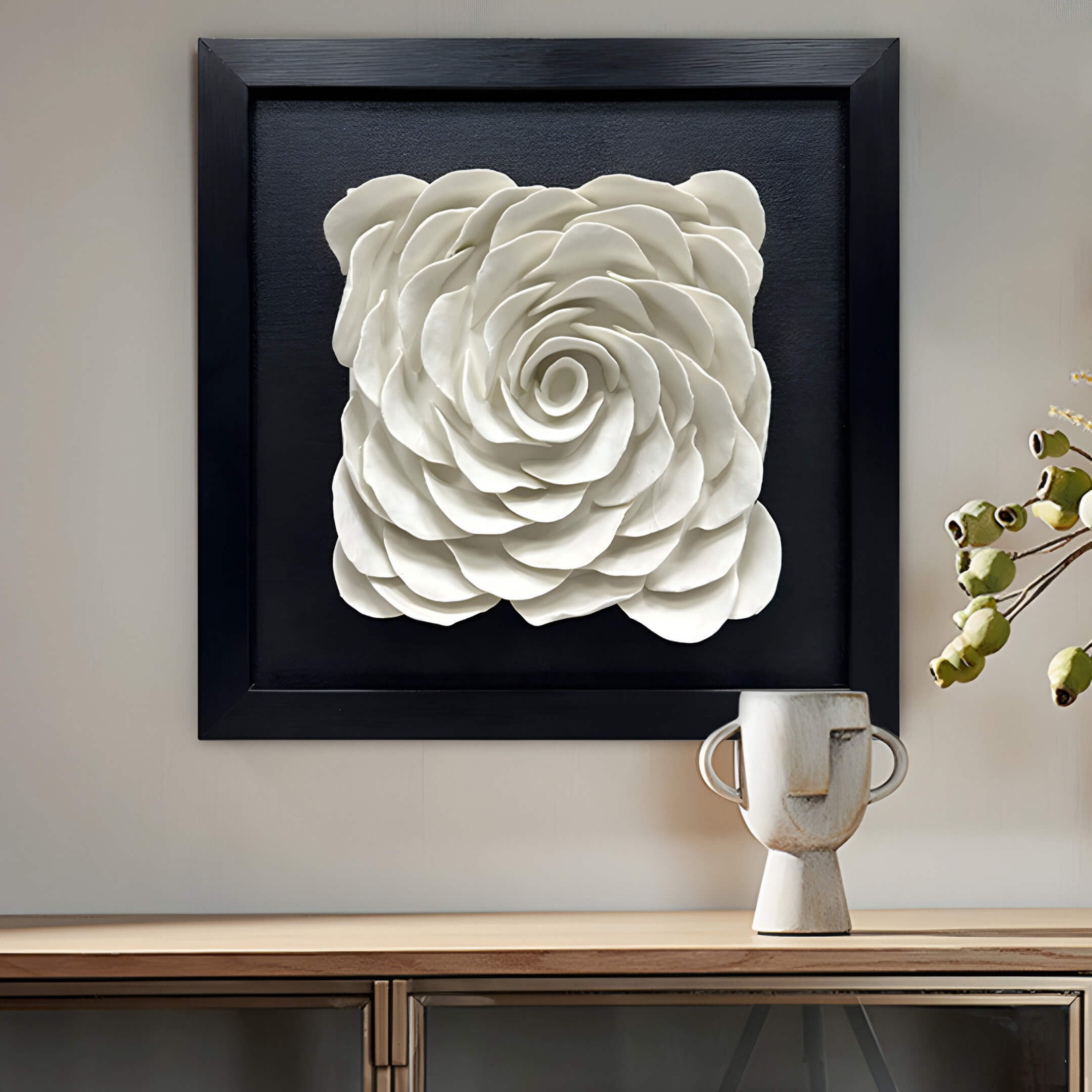 Giant Sculptures Harmonia 3D Rose Wall Installation with Black Frame serves as the centerpiece of modern decor, complemented below by a wooden surface featuring a white artistic vase adorned with branches and small green fruits for an elegant, natural ambiance.