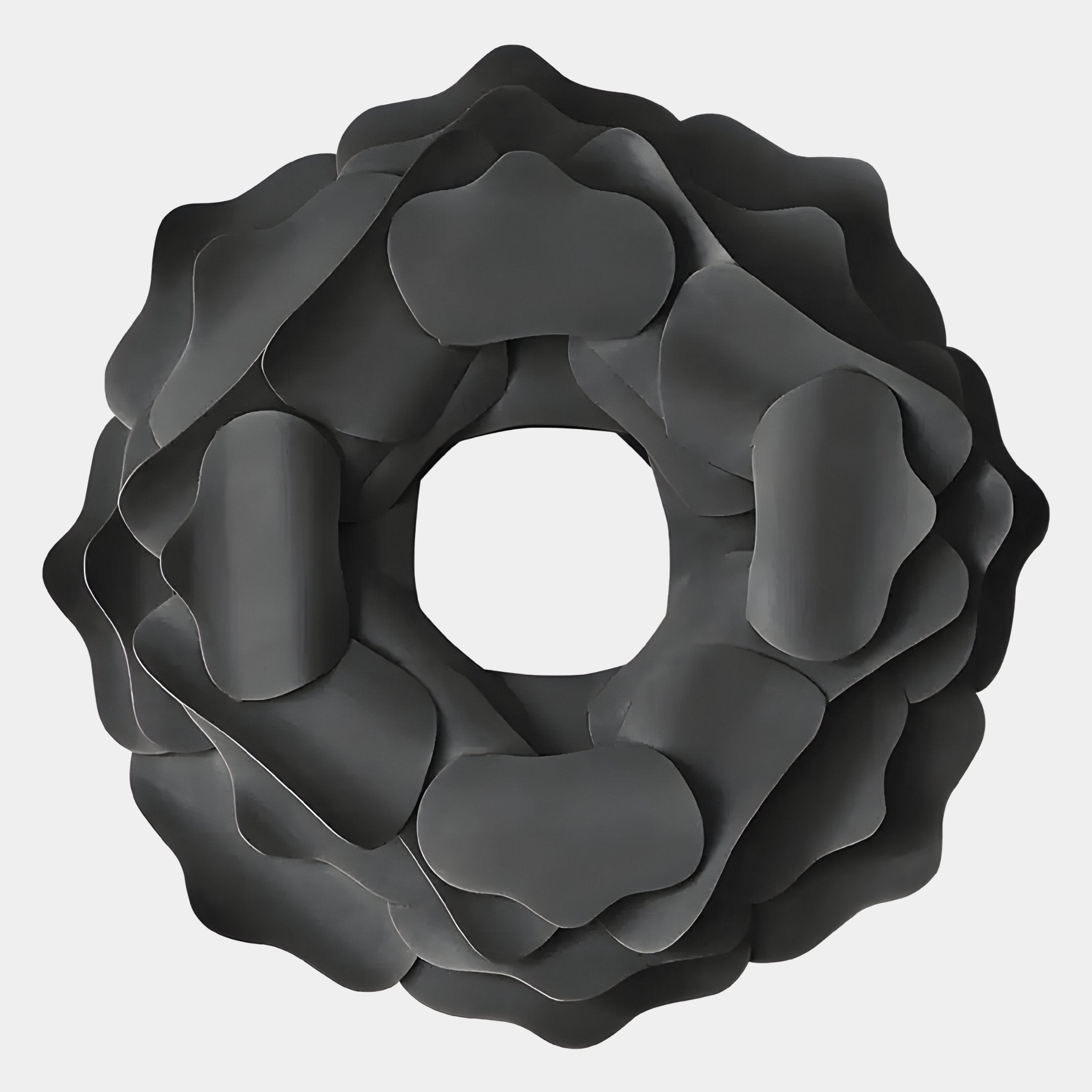 The Sculptura Mirror Charcoal Grey Floral Round Metal Wall Art by Giant Sculptures features overlapping dark gray, rounded forms in a flower-like pattern with a hollow center, set against a light background.