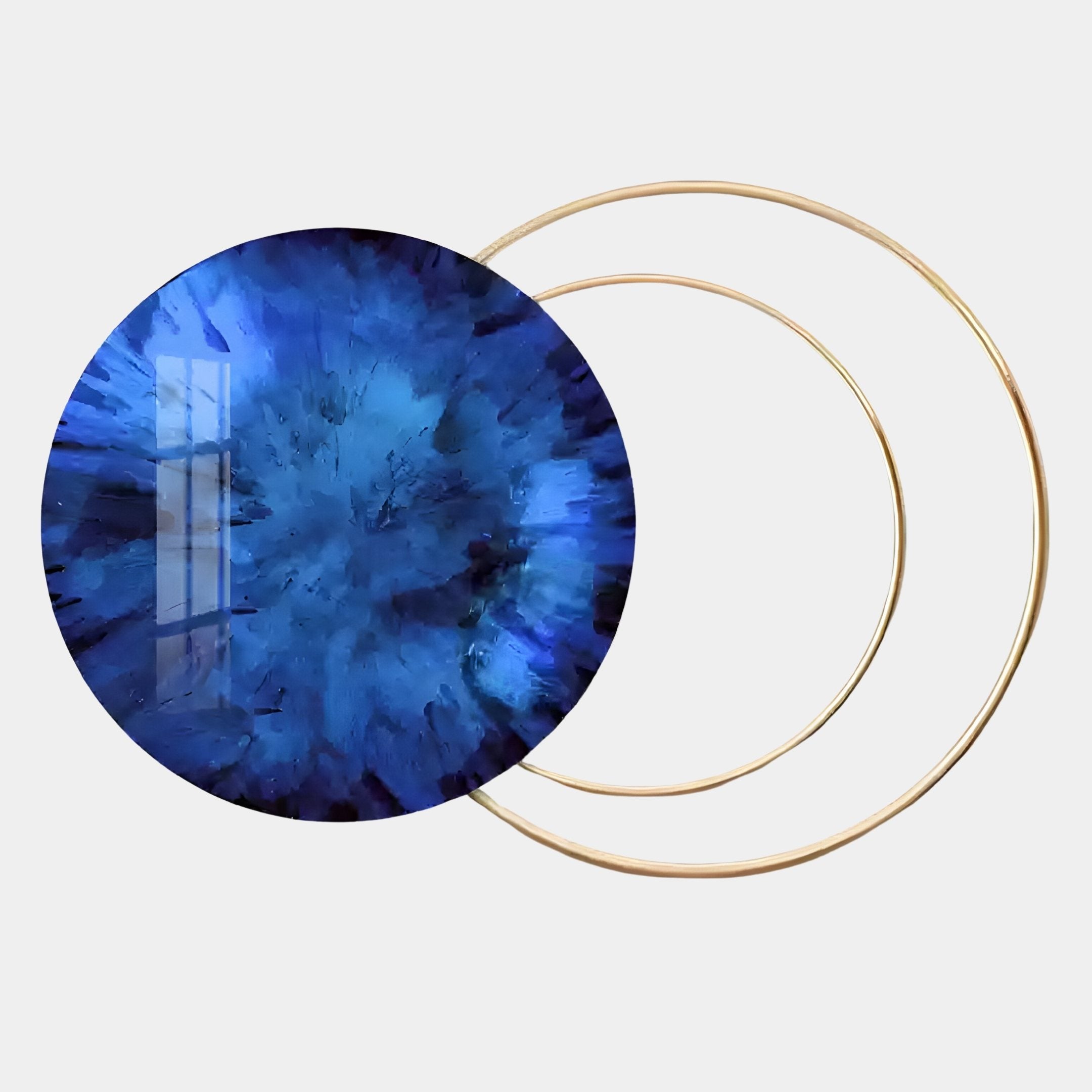 The Eclipse Luxe Sapphire Blue Circular Ring Wall Art by Giant Sculptures features a large, round sapphire blue gem with a radiant pattern, partially overlapping two thin gold rings—perfect for modern interiors.