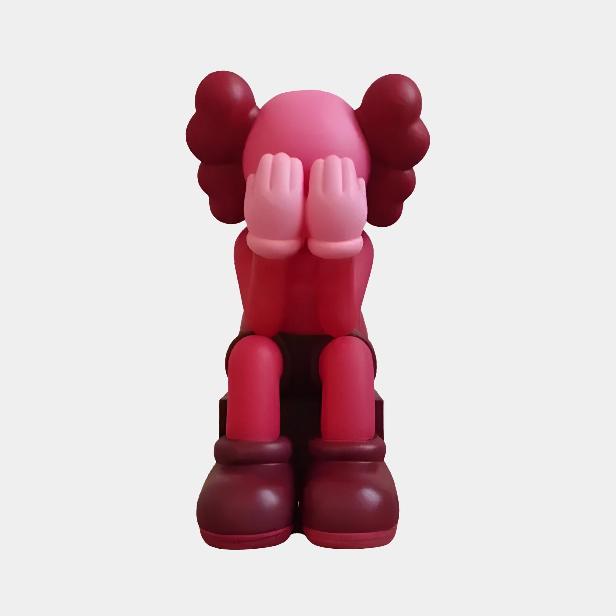 The Giant Sculptures Blush Ruby Iconify Melancholy Sitting Figure - 28cm is a cartoonish resin sculpture featuring a sitting figure with exaggerated gloves and shoes, its face hidden in its hands. It has iconic charm, with large round shapes resembling ears or hair enhancing the design.
