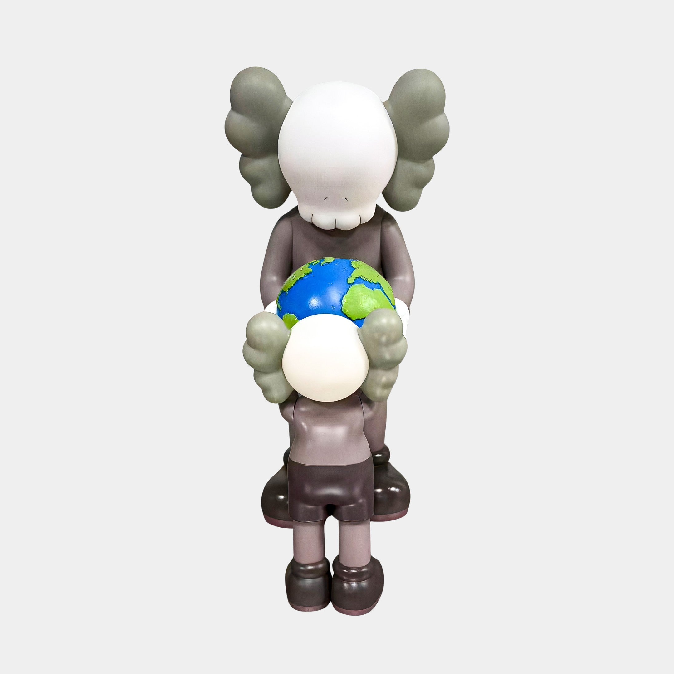 The Hazelnut Brown Iconify Atlas Figure - 30cm by Giant Sculptures features two cartoon-style, skull-headed figures on a plain white background; the taller figure hands a small globe to the shorter, making it ideal symbolic home office decor.
